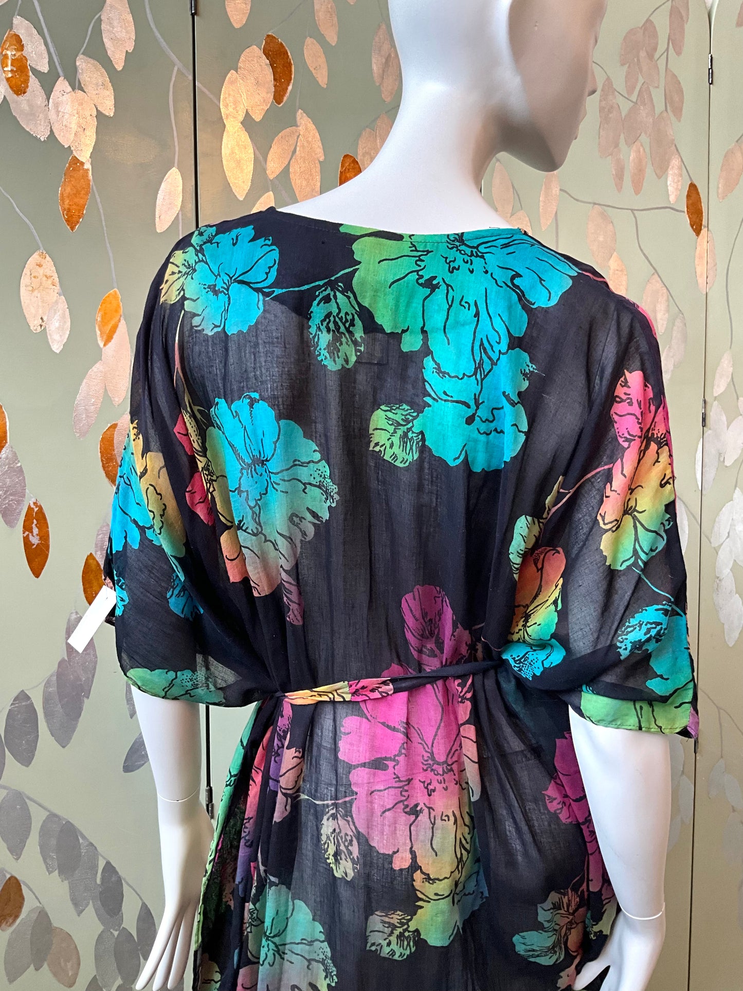 Mannequin wearing a colorful floral dress against a patterned wall.