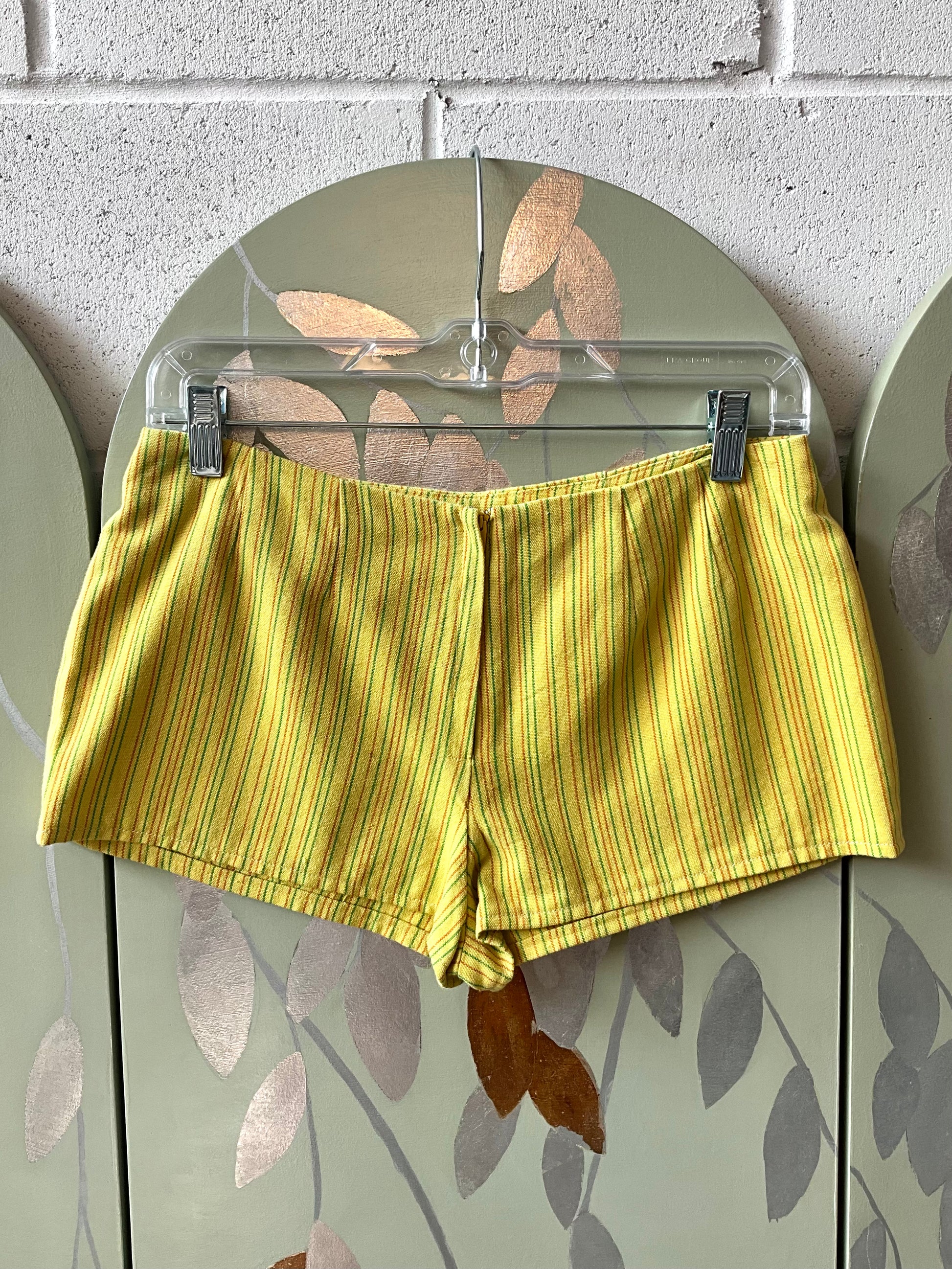 Yellow striped shorts on a hanger against a brick wall.