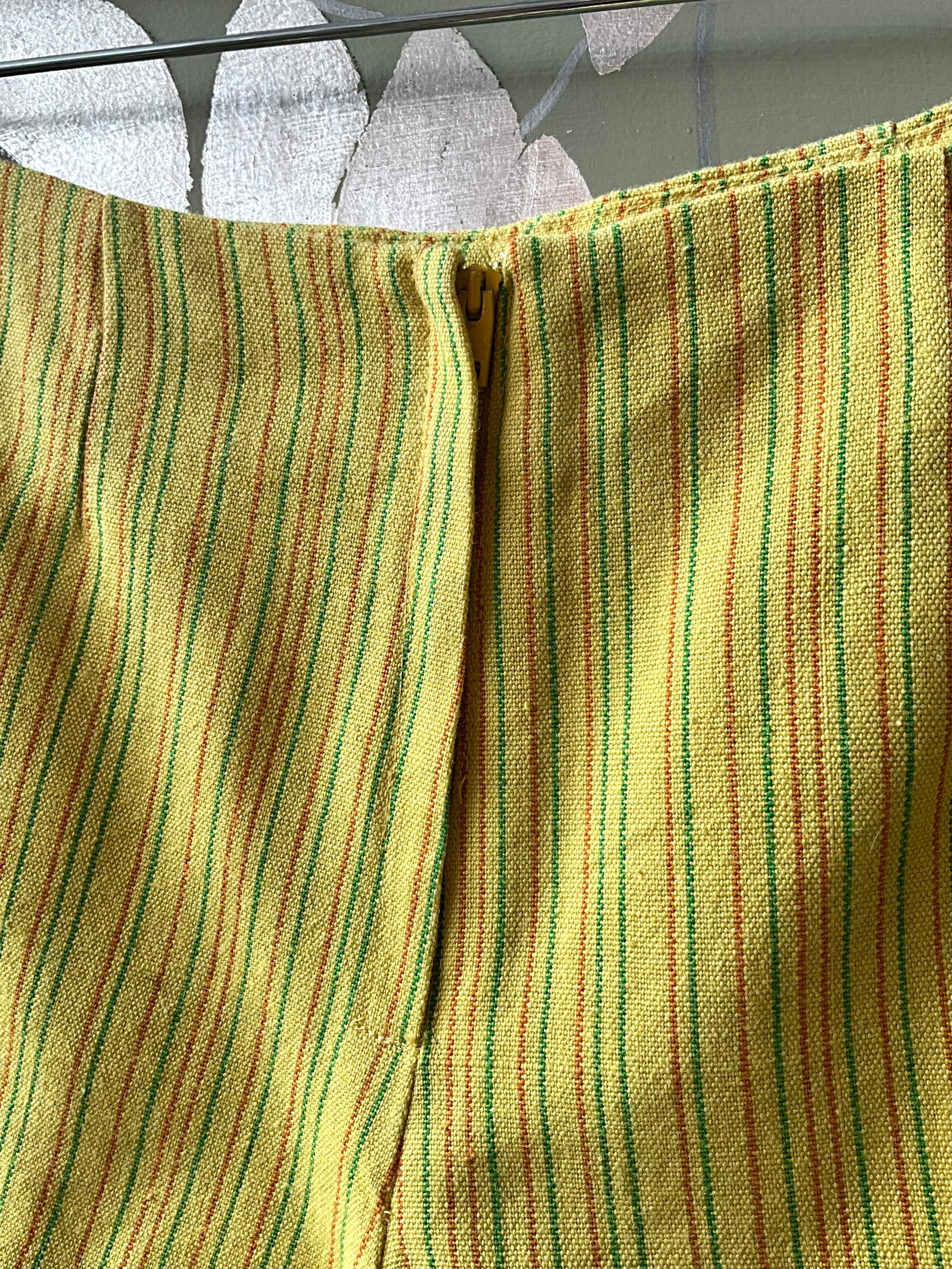 Close-up of a yellow and green striped fabric and zipper from a pair of shorts. 