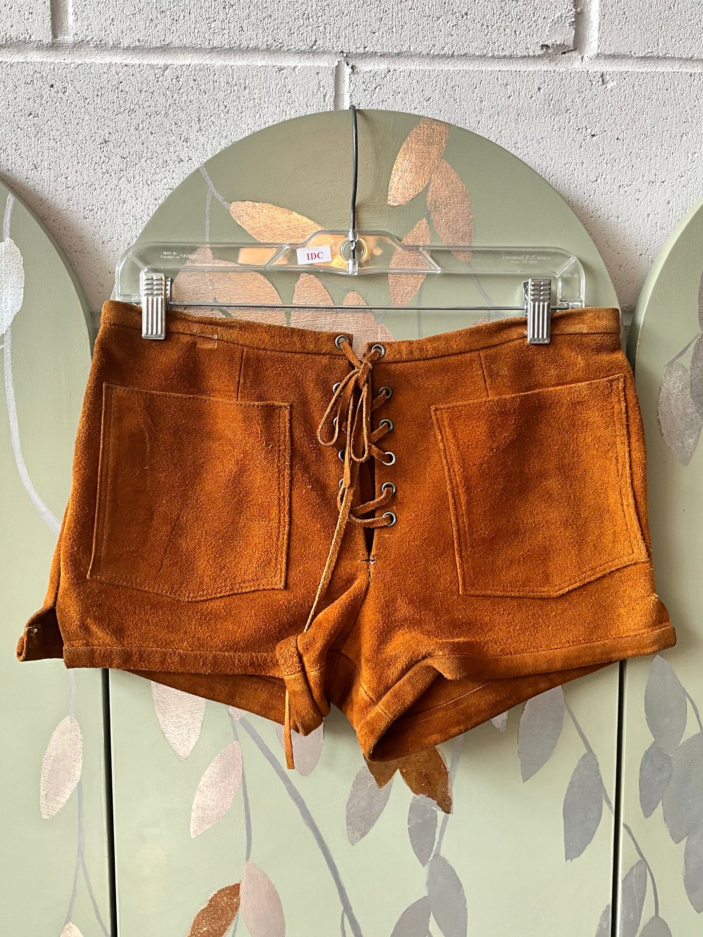 Brown suede shorts on a hanger against a floral-patterned wall.