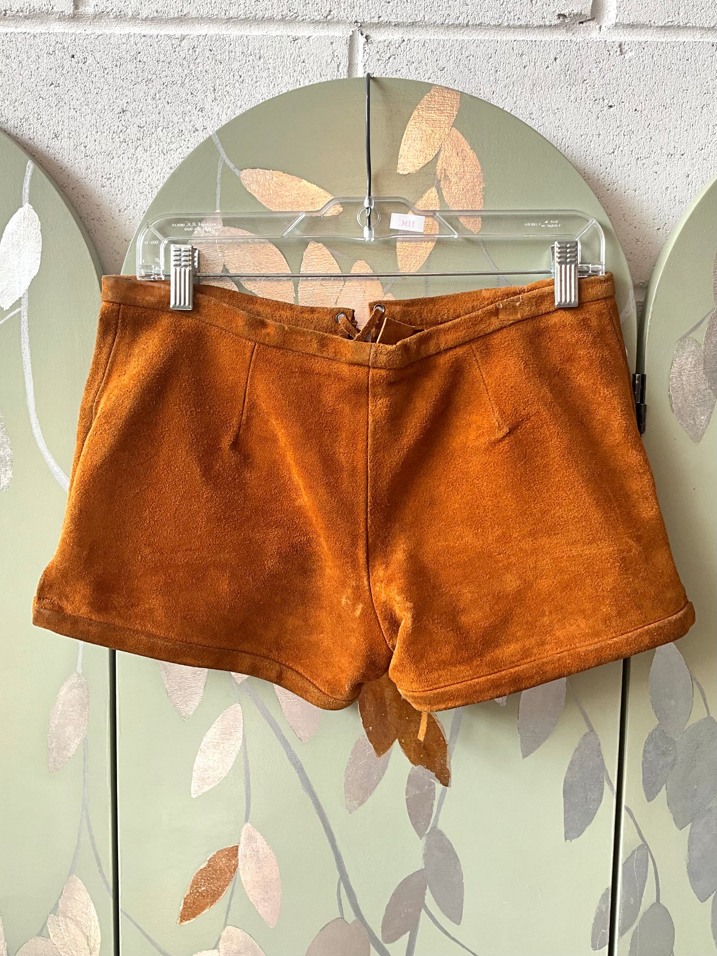 Brown shorts on a hanger against a light green wall with leaf patterns