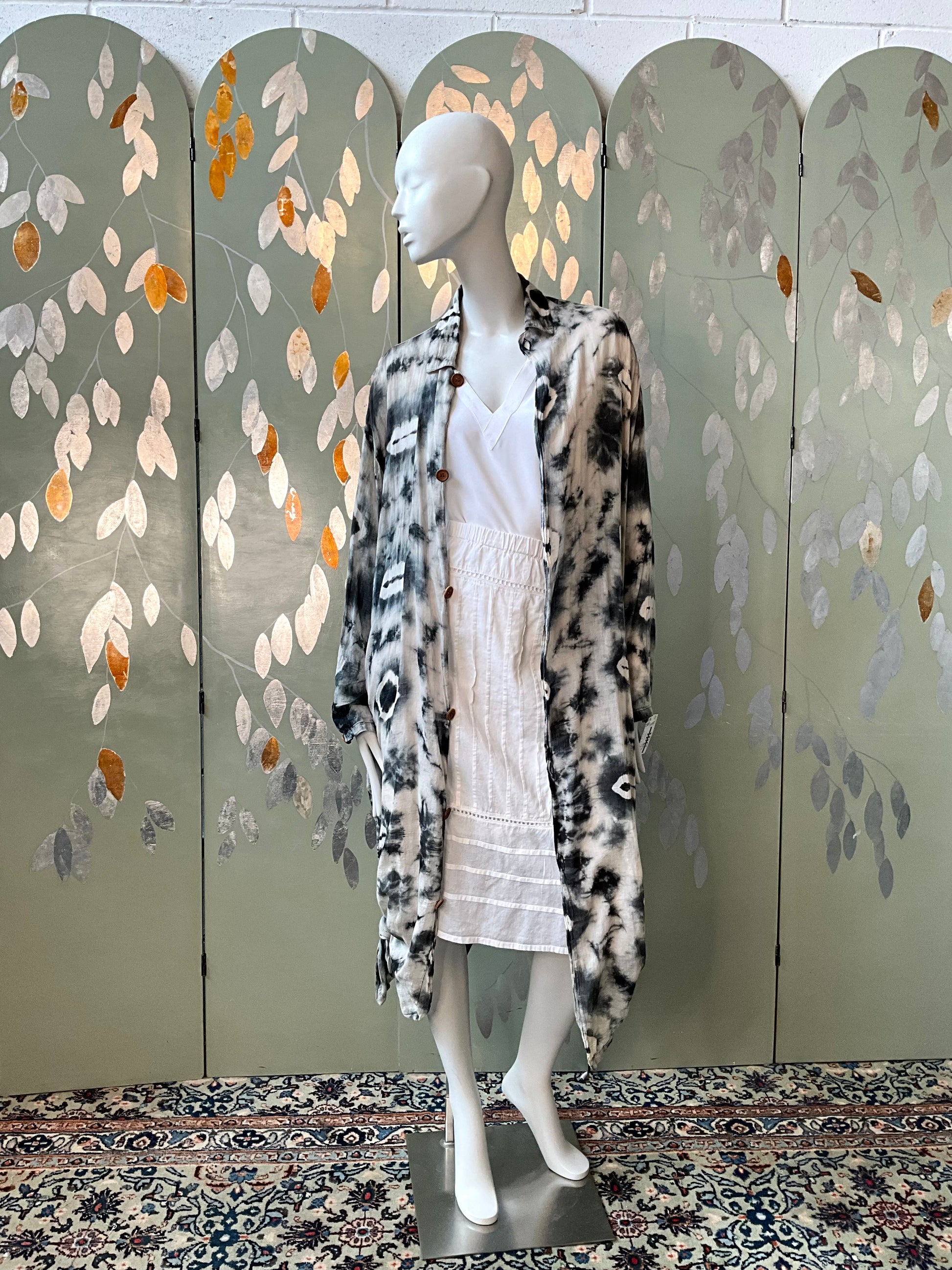 Mannequin wearing a patterned coat in front of a decorative screen with leaf designs.