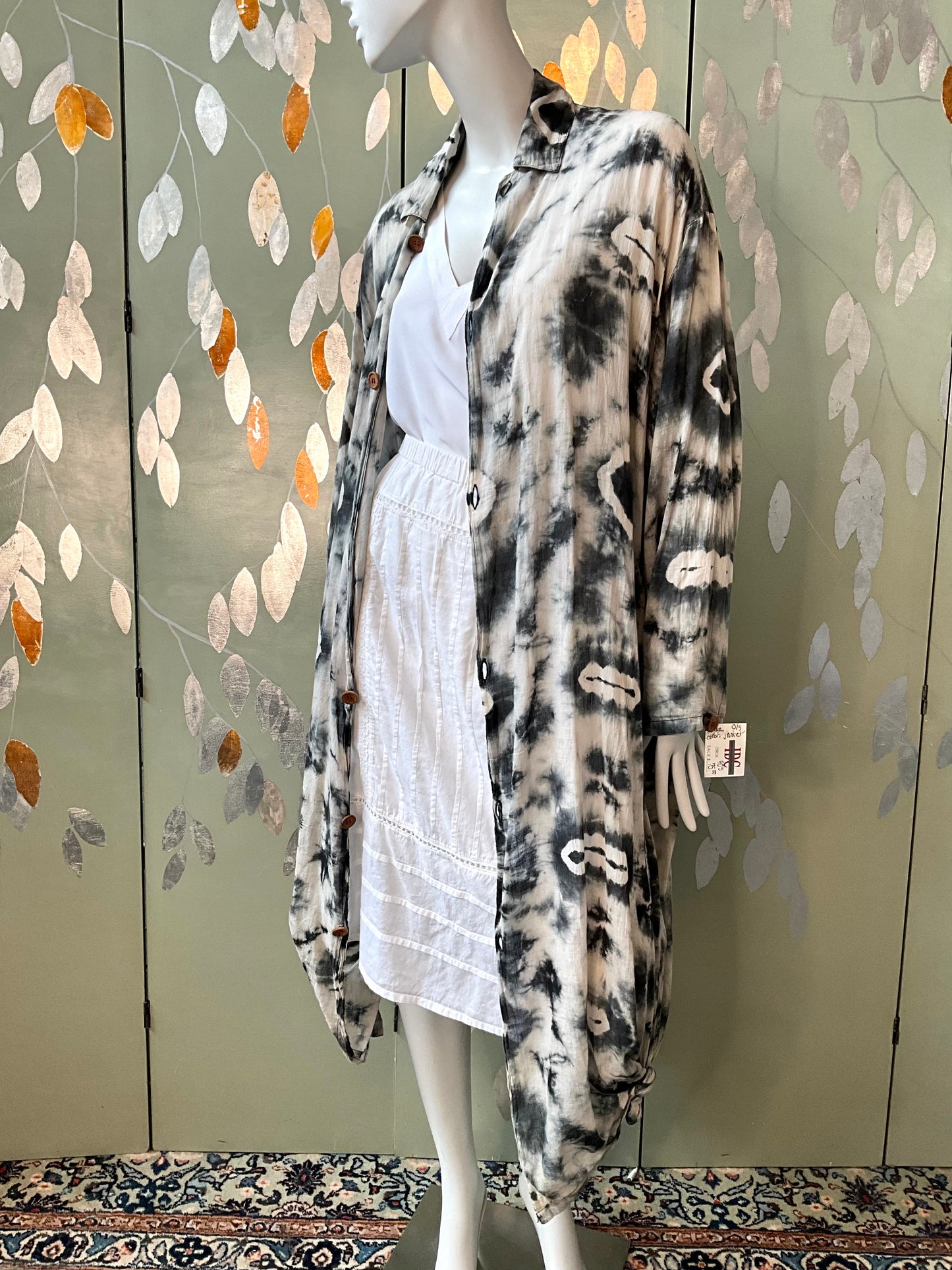 Mannequin wearing a tie-dye cardigan over a white dress against a decorative wall.