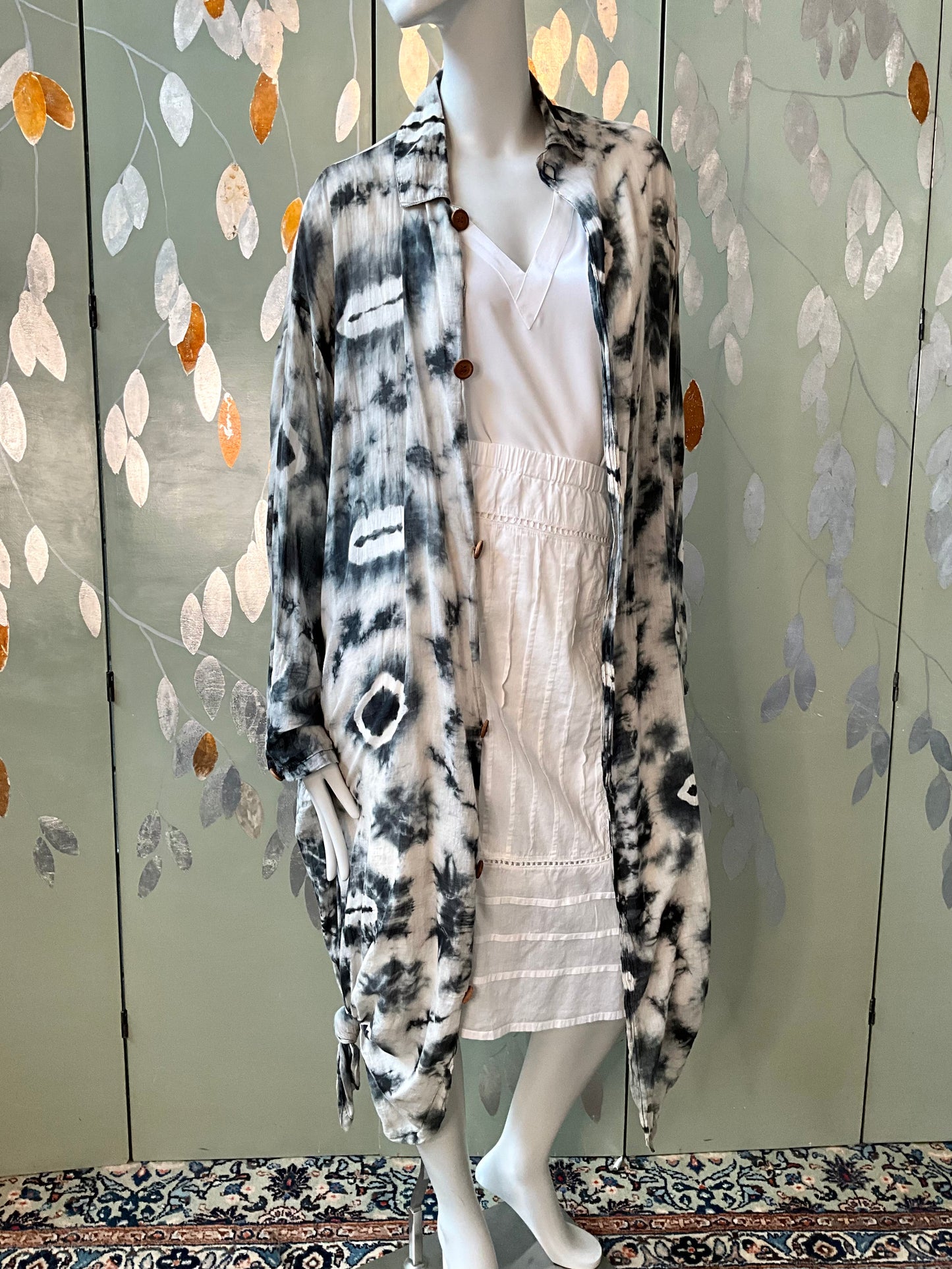Mannequin wearing a long, patterned cardigan in front of a decorative wall.