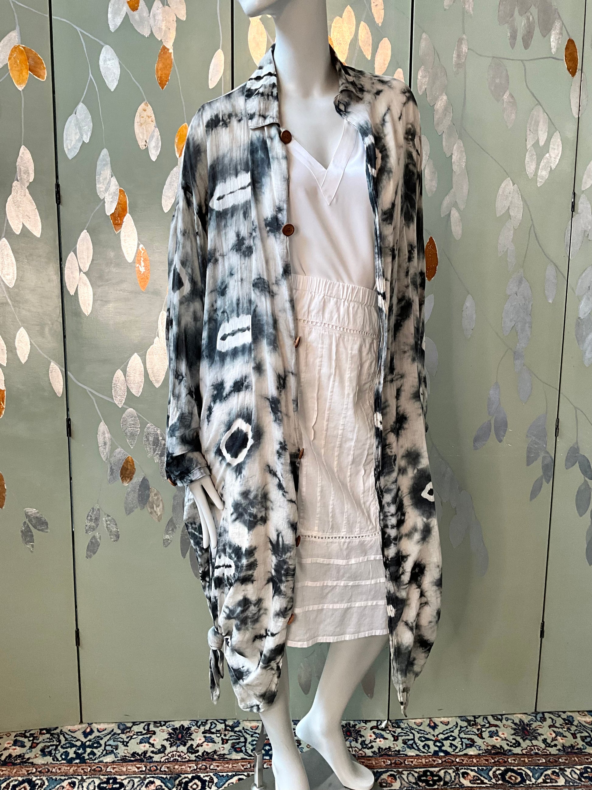 Mannequin wearing a long, patterned cardigan in front of a decorative wall.