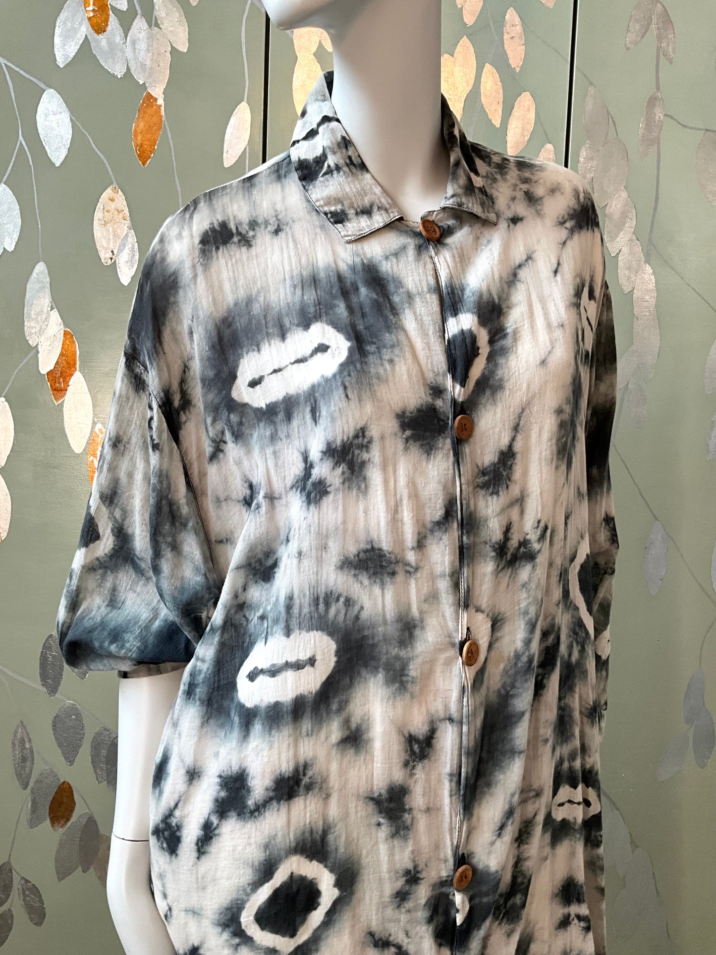 Mannequin wearing a tie-dye shirt with abstract patterns against a decorative wall.