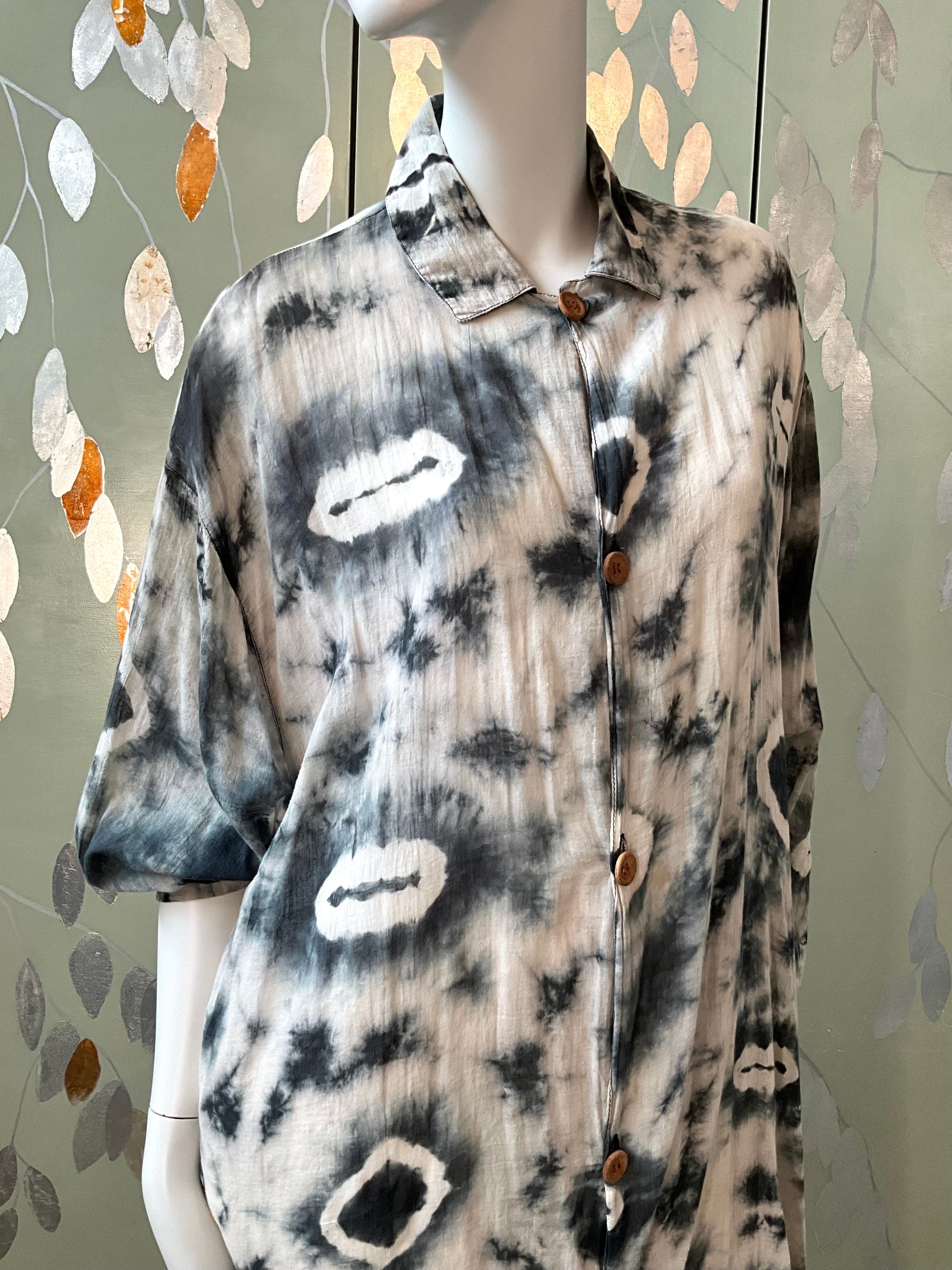 Mannequin wearing a tie-dye shirt with abstract patterns against a decorative wall.