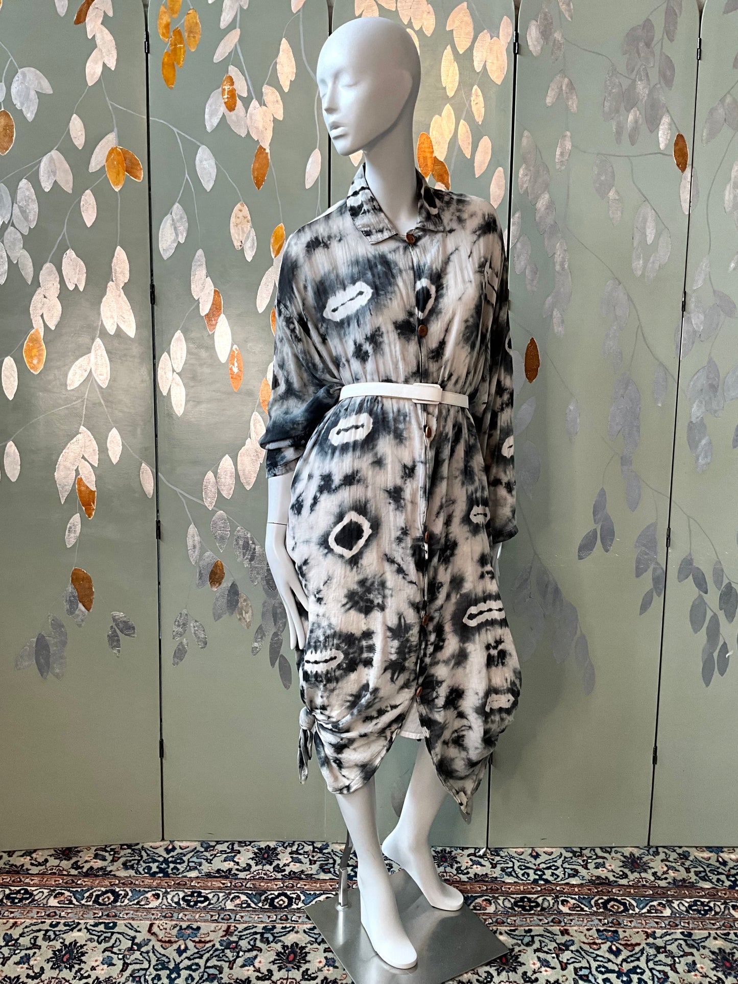 Mannequin wearing a patterned dress against a decorative wall with leaf designs.