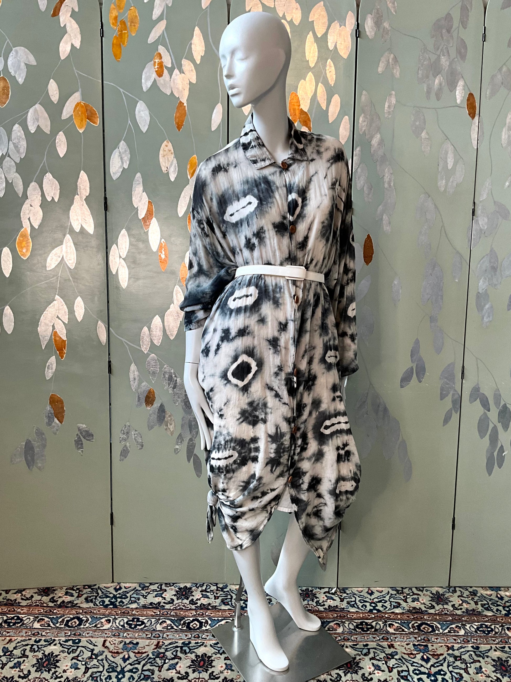 Mannequin wearing a patterned dress against a decorative wall with leaf designs.