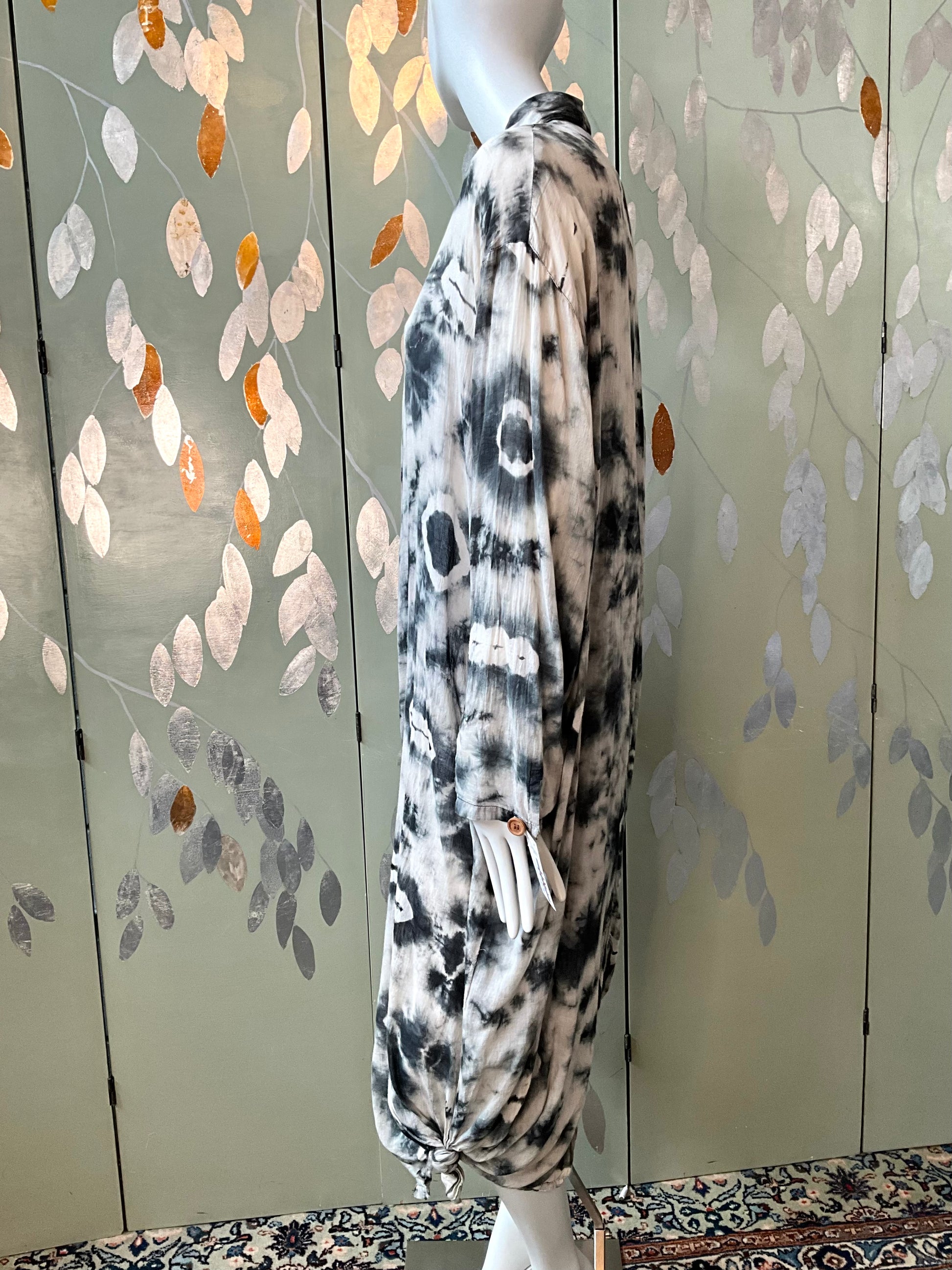 Mannequin wearing a patterned outfit against a decorative wall with leaf designs.