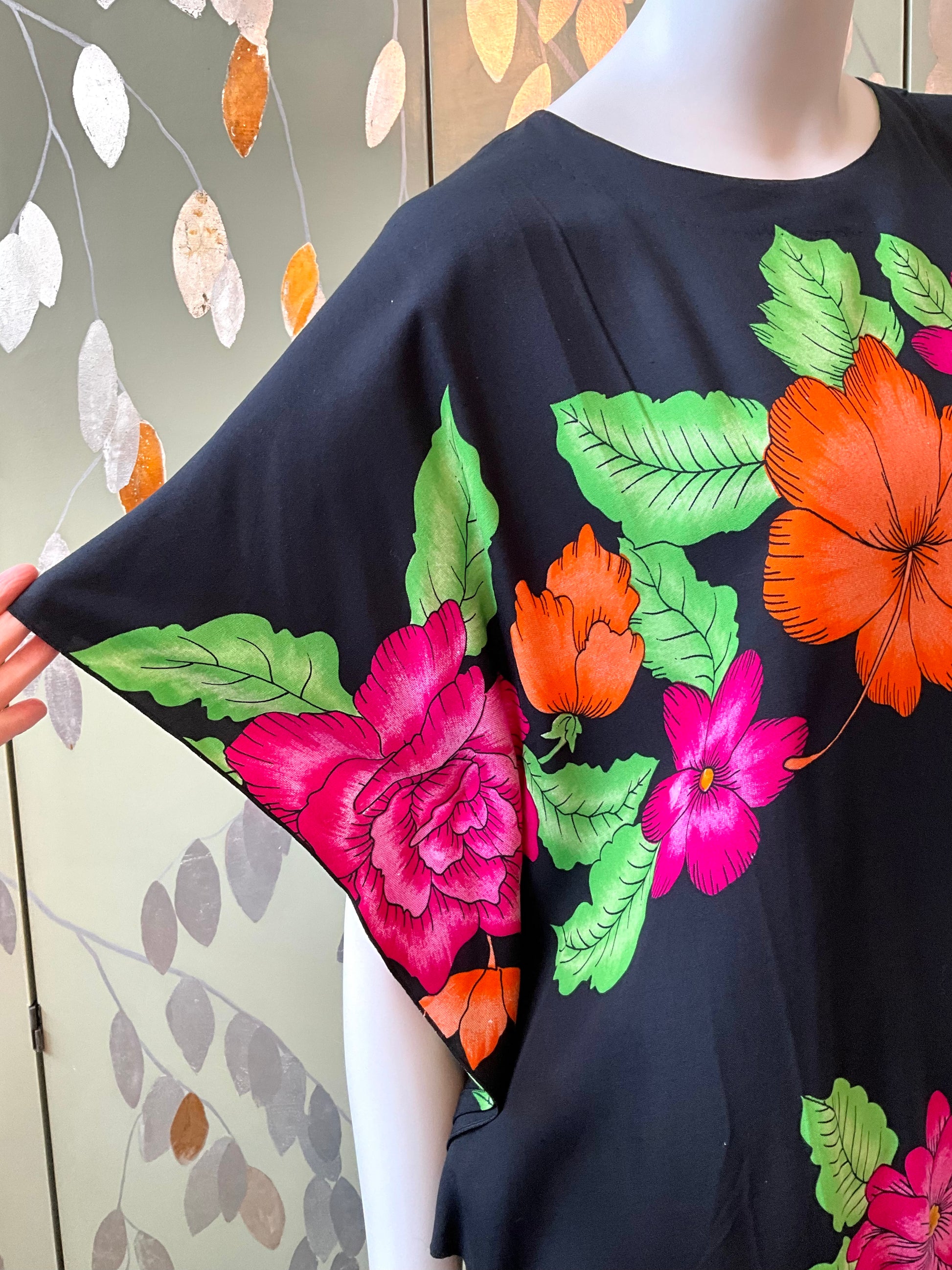 Black dress with colorful floral designs on a mannequin against a patterned wall.