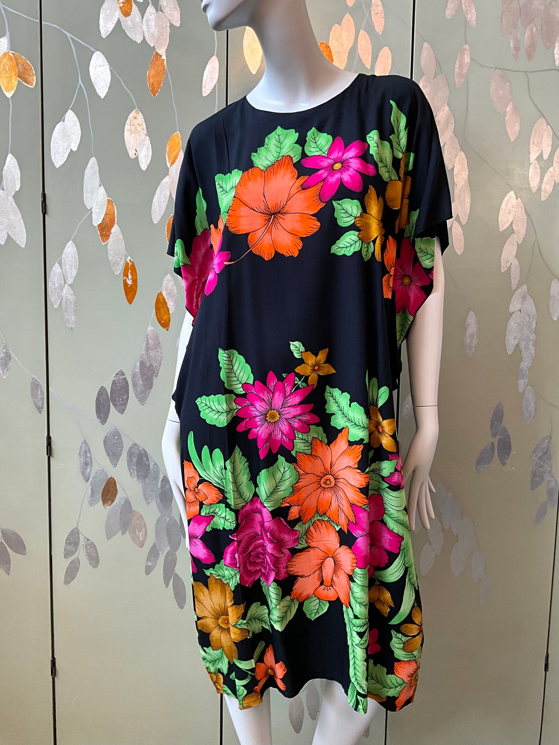 Mannequin wearing a black dress with colorful floral patterns against a decorative wall.
