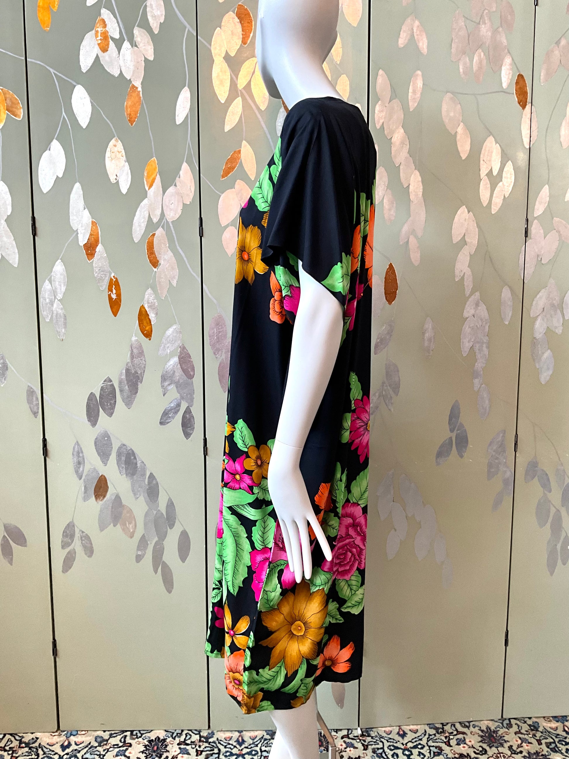 Mannequin wearing a black dress with colorful floral patterns against a decorative wall.
