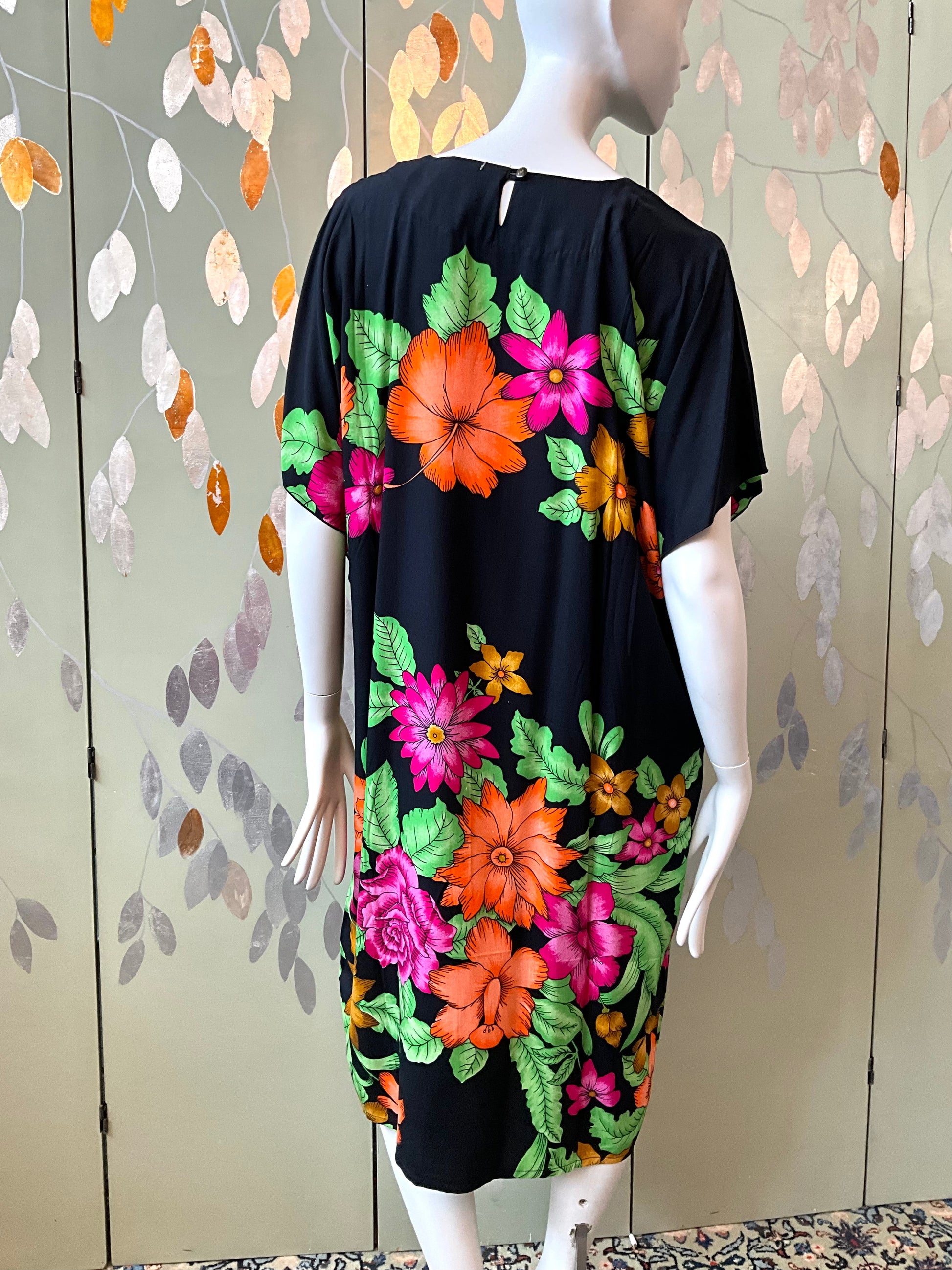 Mannequin wearing a black dress with colorful floral patterns against a patterned wall.