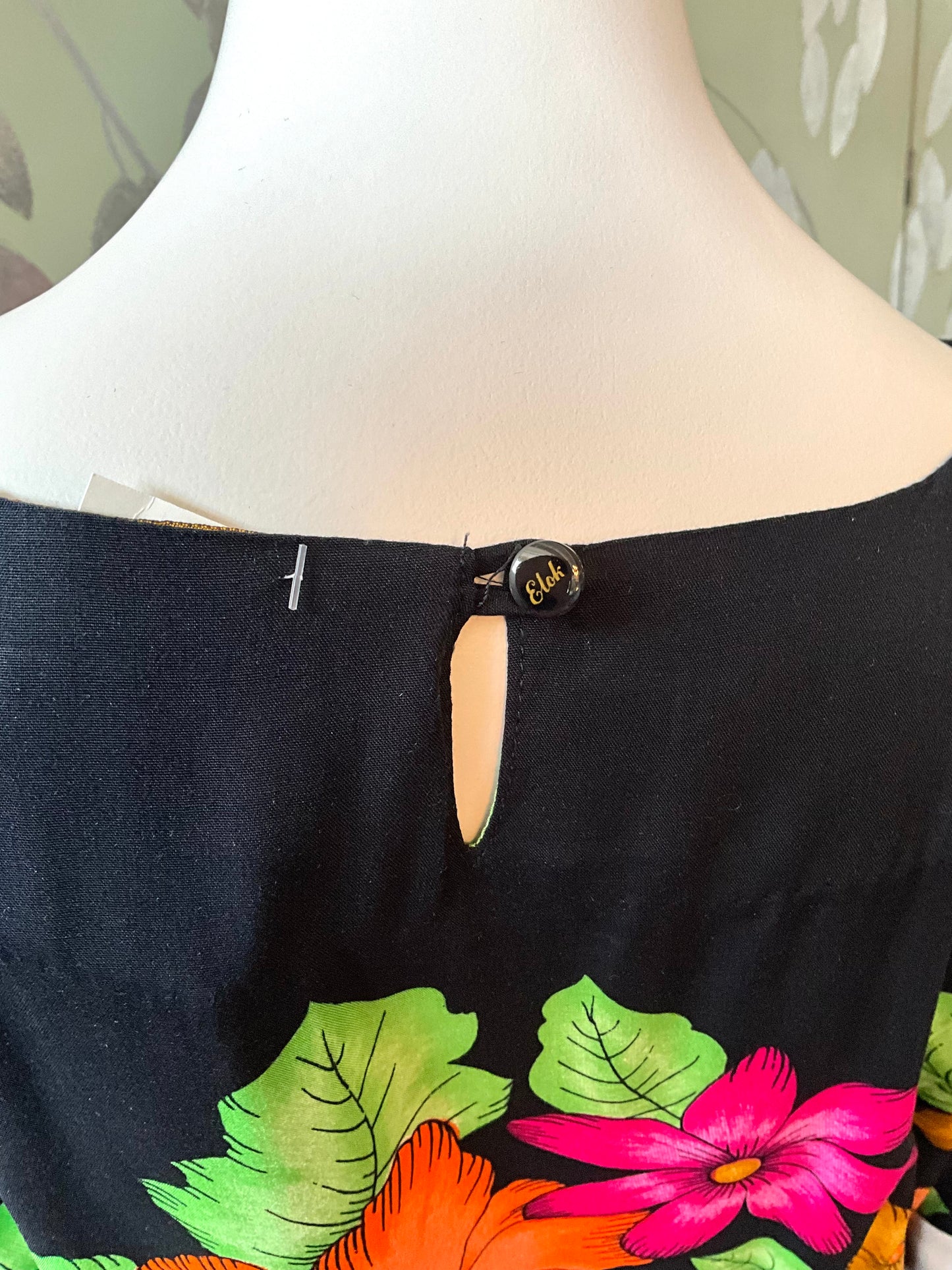 Black dress neckline with colorful floral design on a mannequin against a neutral background