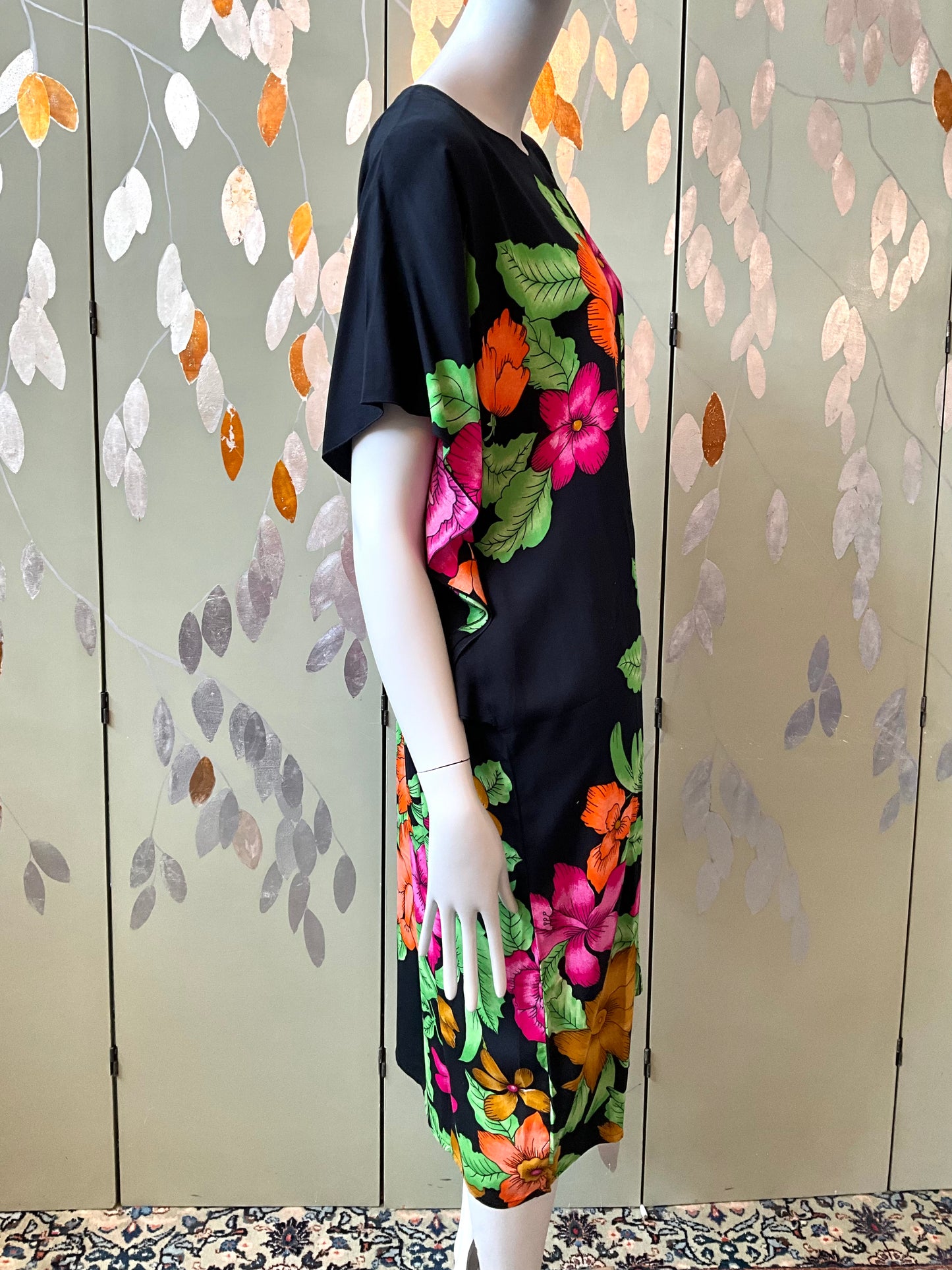 Mannequin wearing a black dress with colorful floral patterns against a decorative wall.
