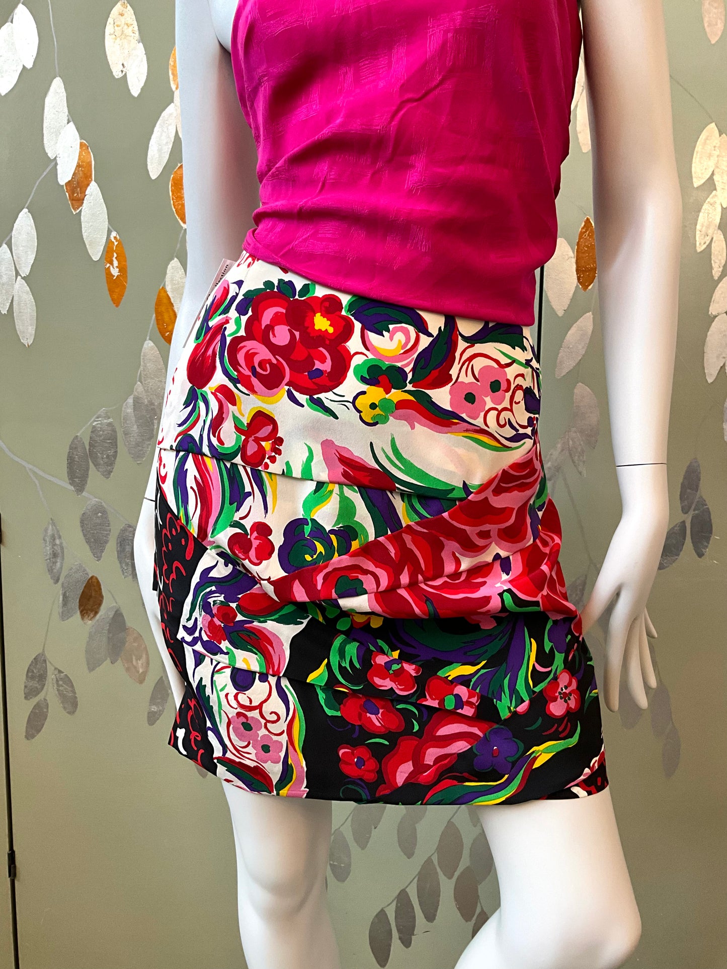 Mannequin wearing a colorful floral skirt and pink top against a patterned background