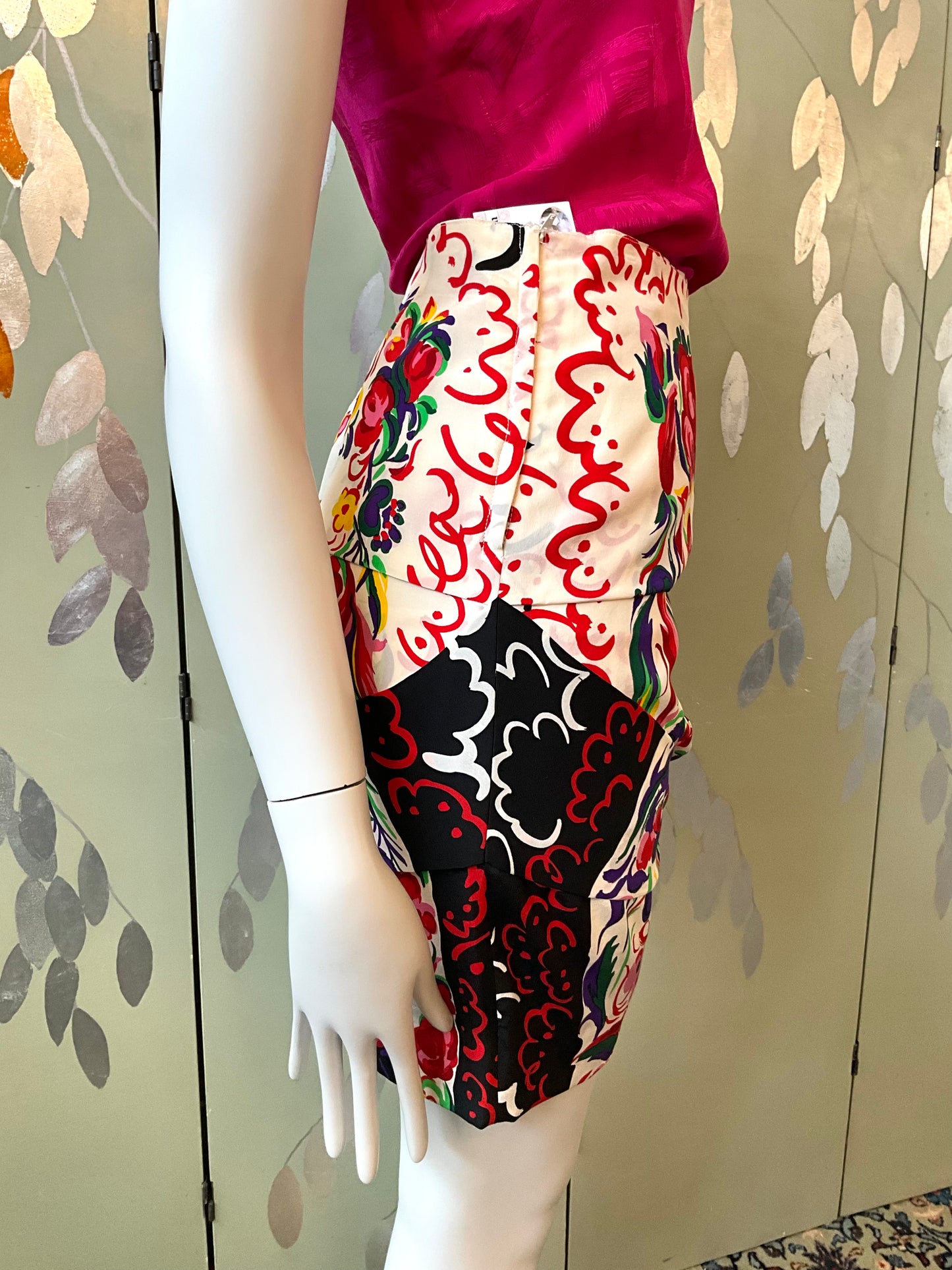 Mannequin wearing a colorful patterned skirt with a floral design against a leafy background