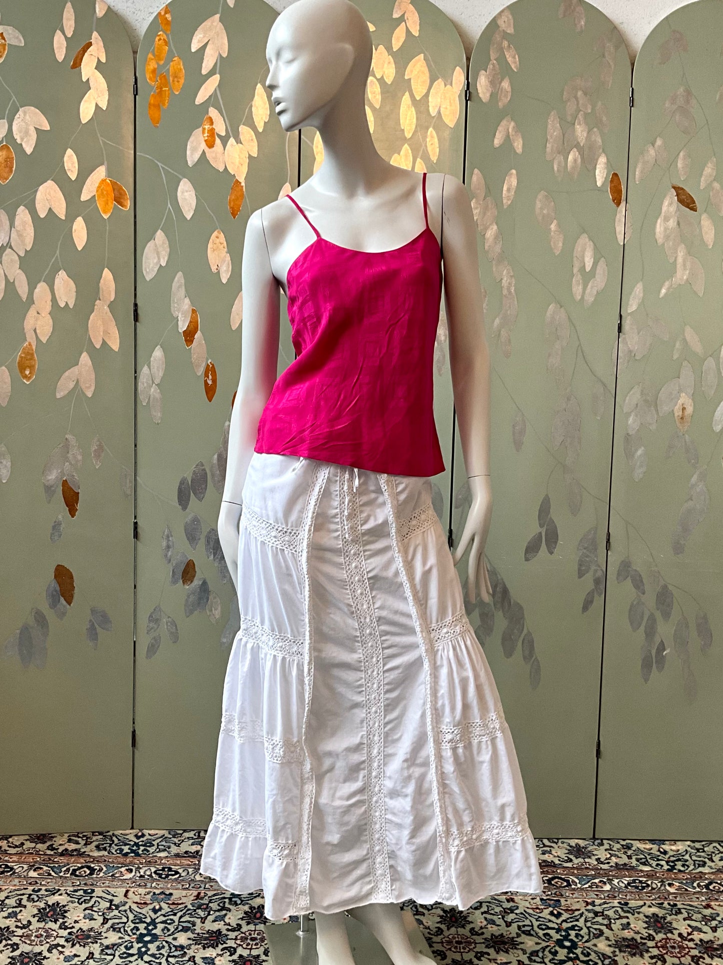 Mannequin wearing a pink top and white skirt against a decorative screen.