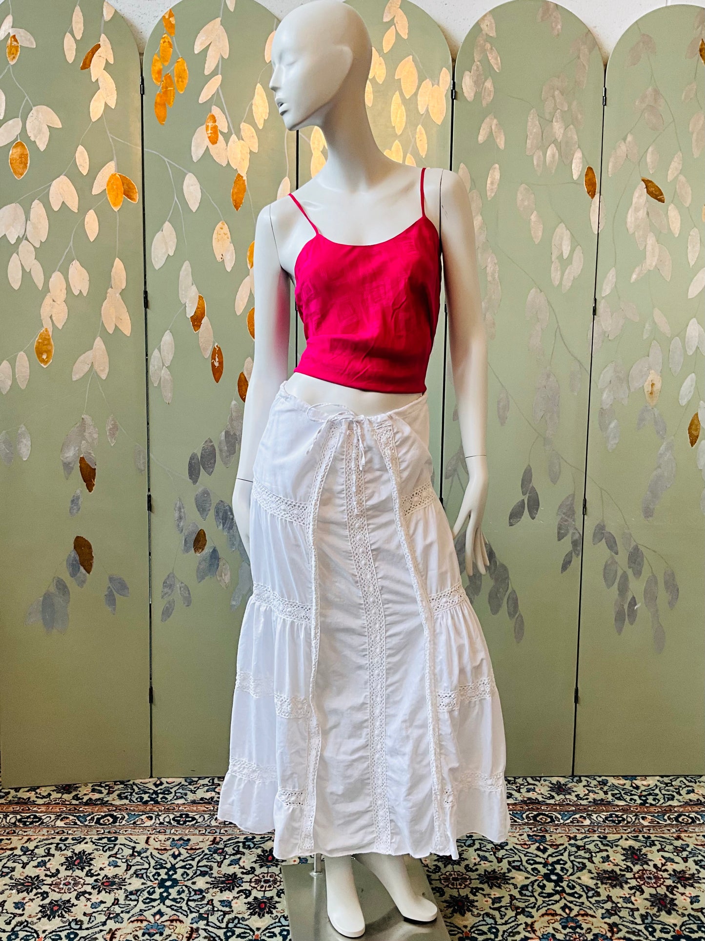 Mannequin wearing a pink top and white skirt against a decorative wall.