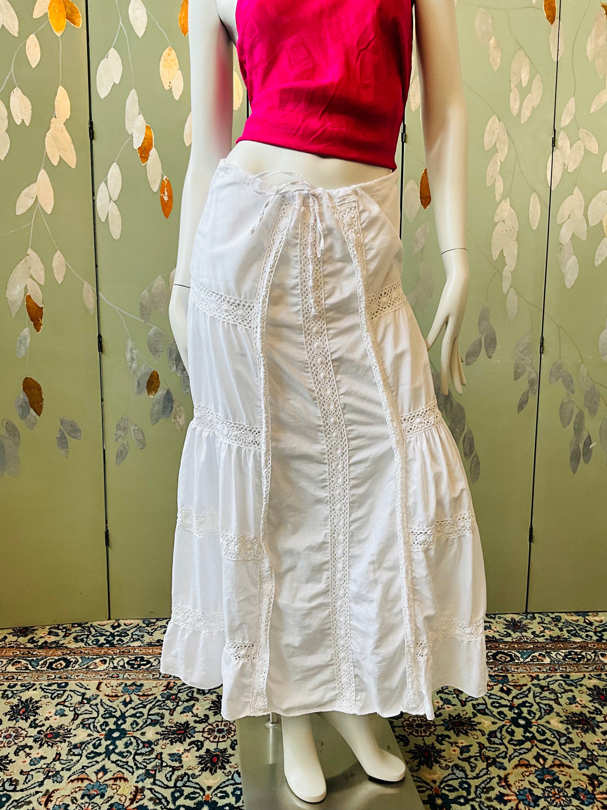 Mannequin wearing a white lace skirt and pink top against a floral wall.