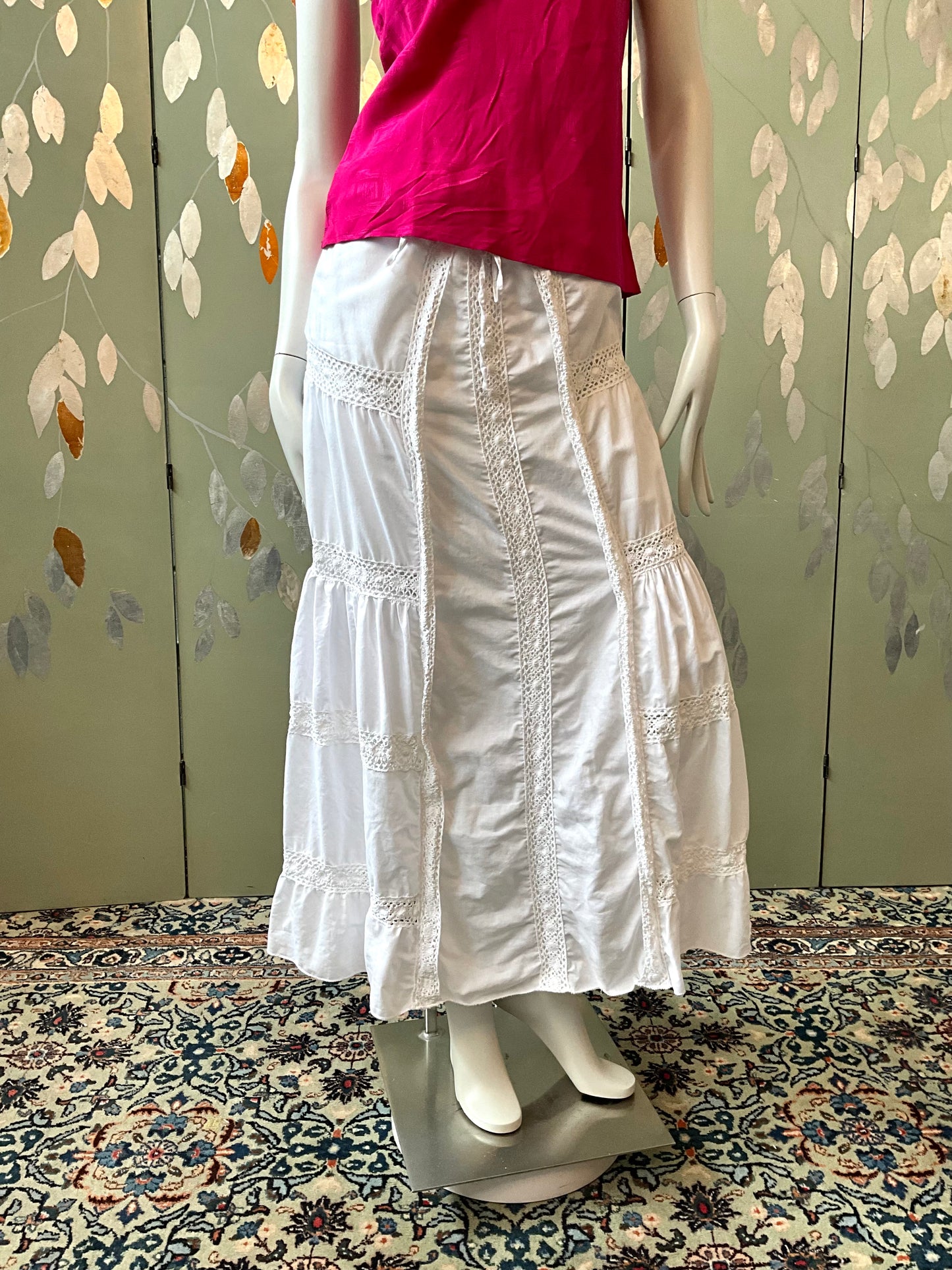Mannequin wearing a white skirt and pink top against a floral-patterned wall.