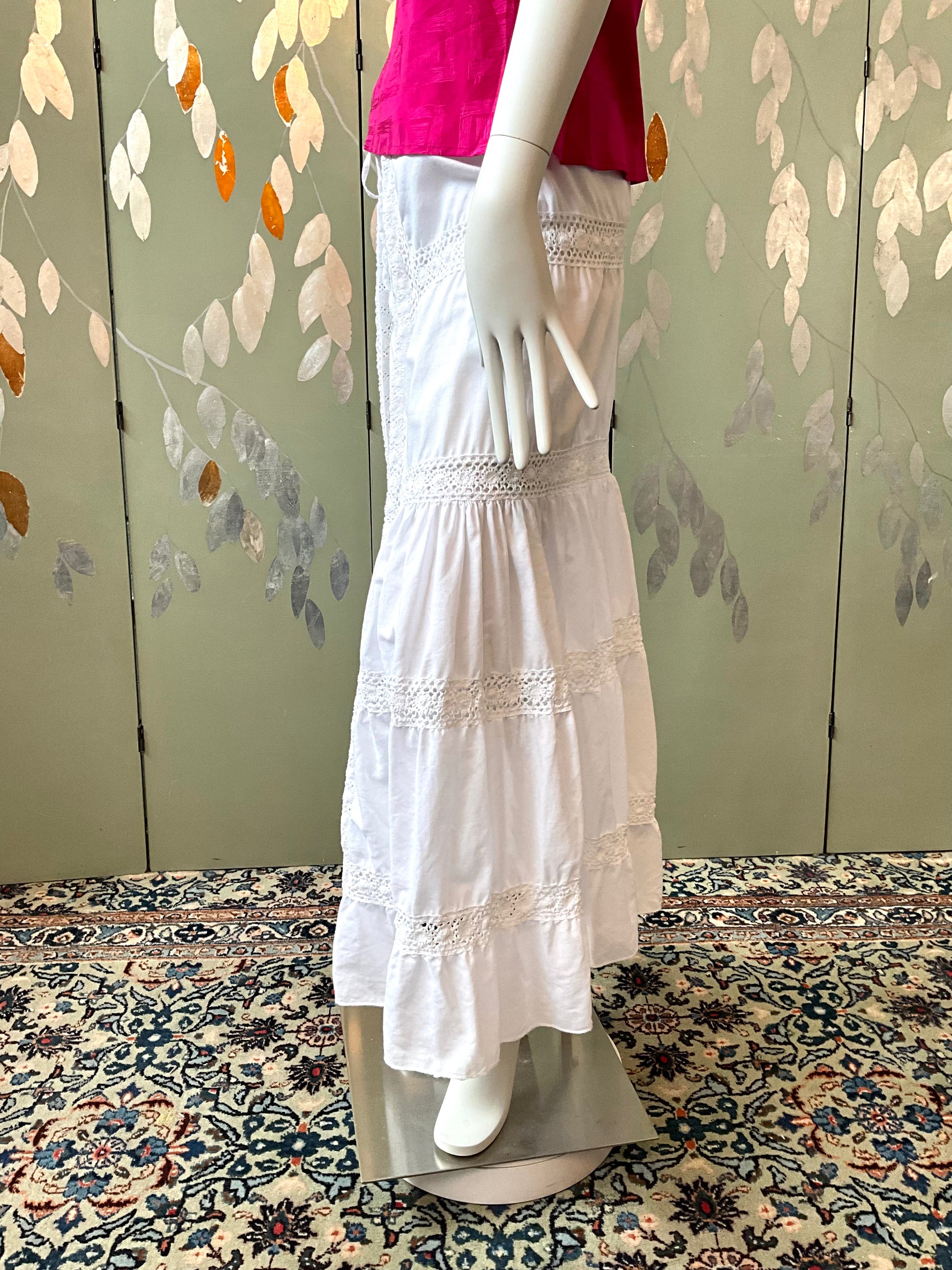 Mannequin wearing a white dress with lace details against a patterned wall.