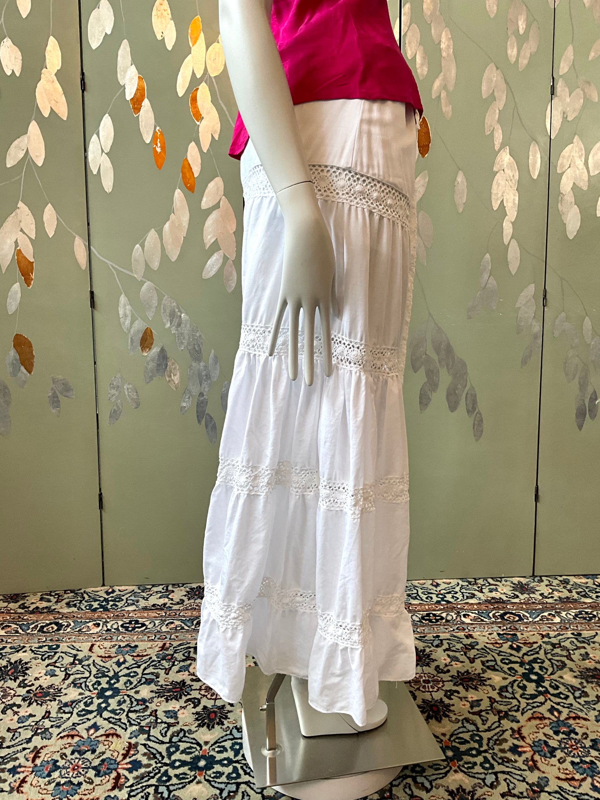Mannequin wearing a white skirt with lace details against a decorative wall.