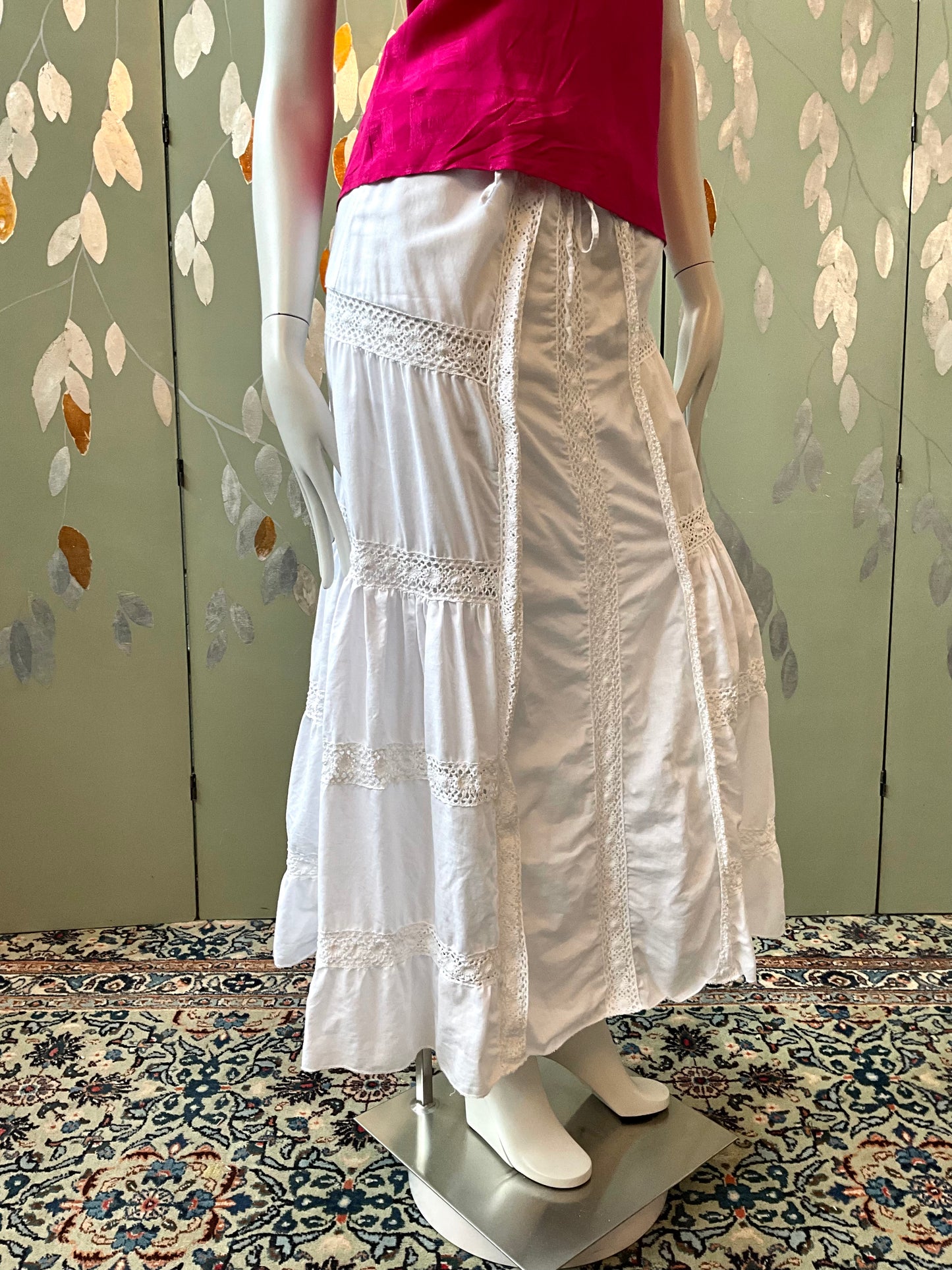 Mannequin wearing a white lace skirt and pink top against a floral-patterned wall.