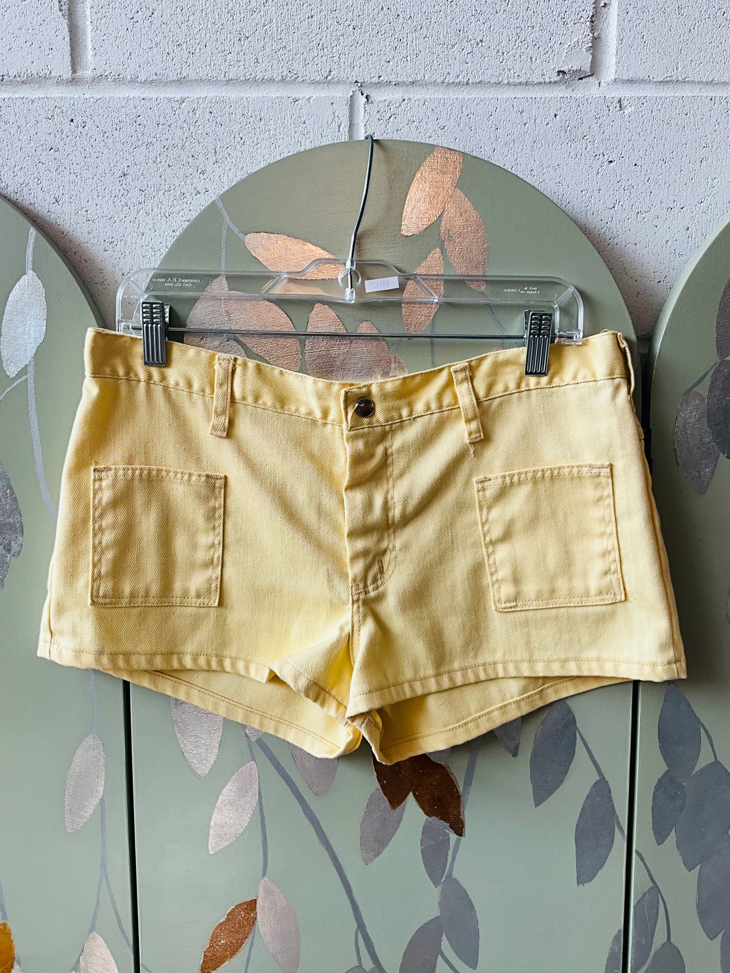 Yellow shorts on a hanger against a brick wall.