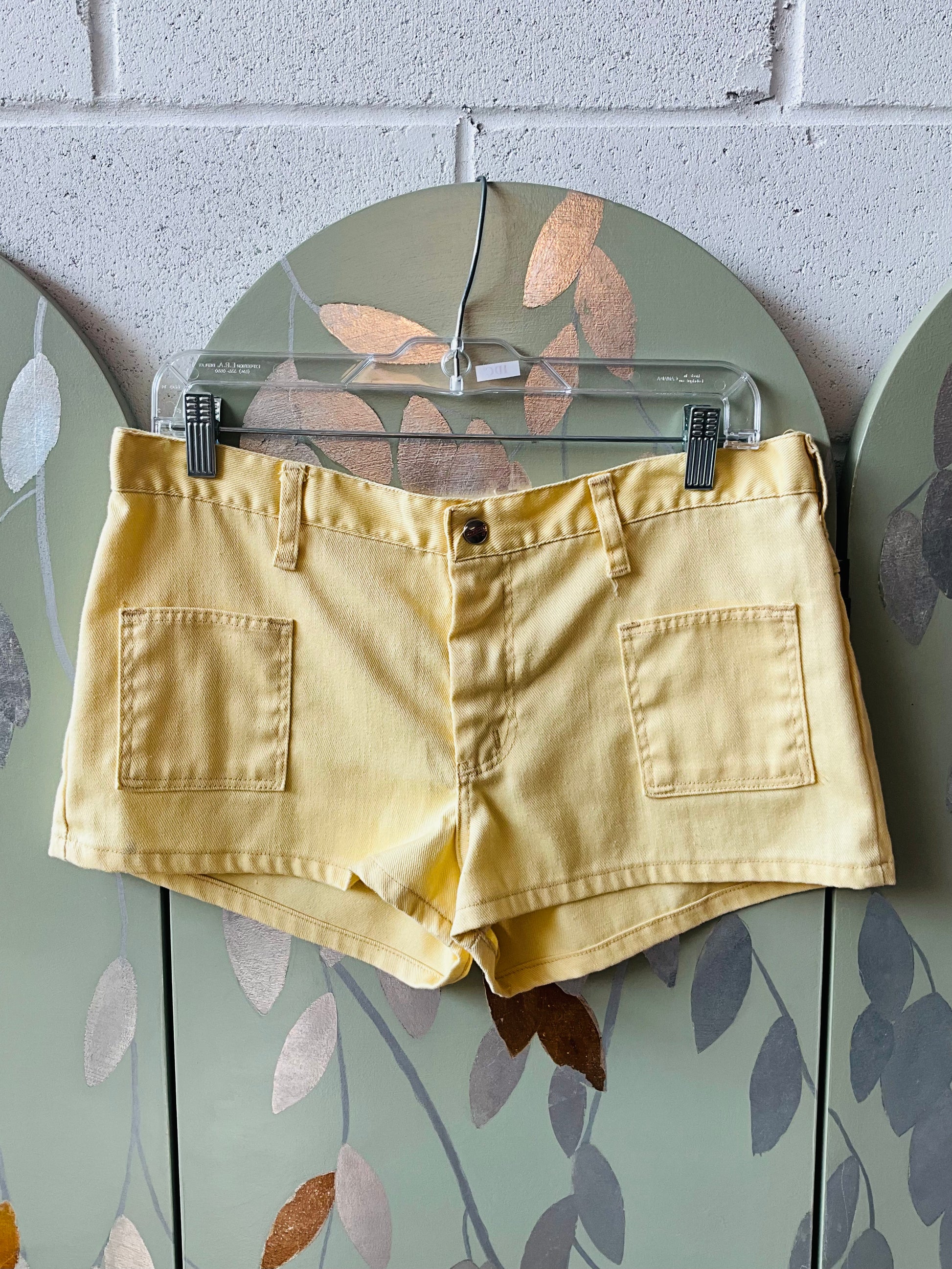 Yellow shorts on a hanger against a brick wall.