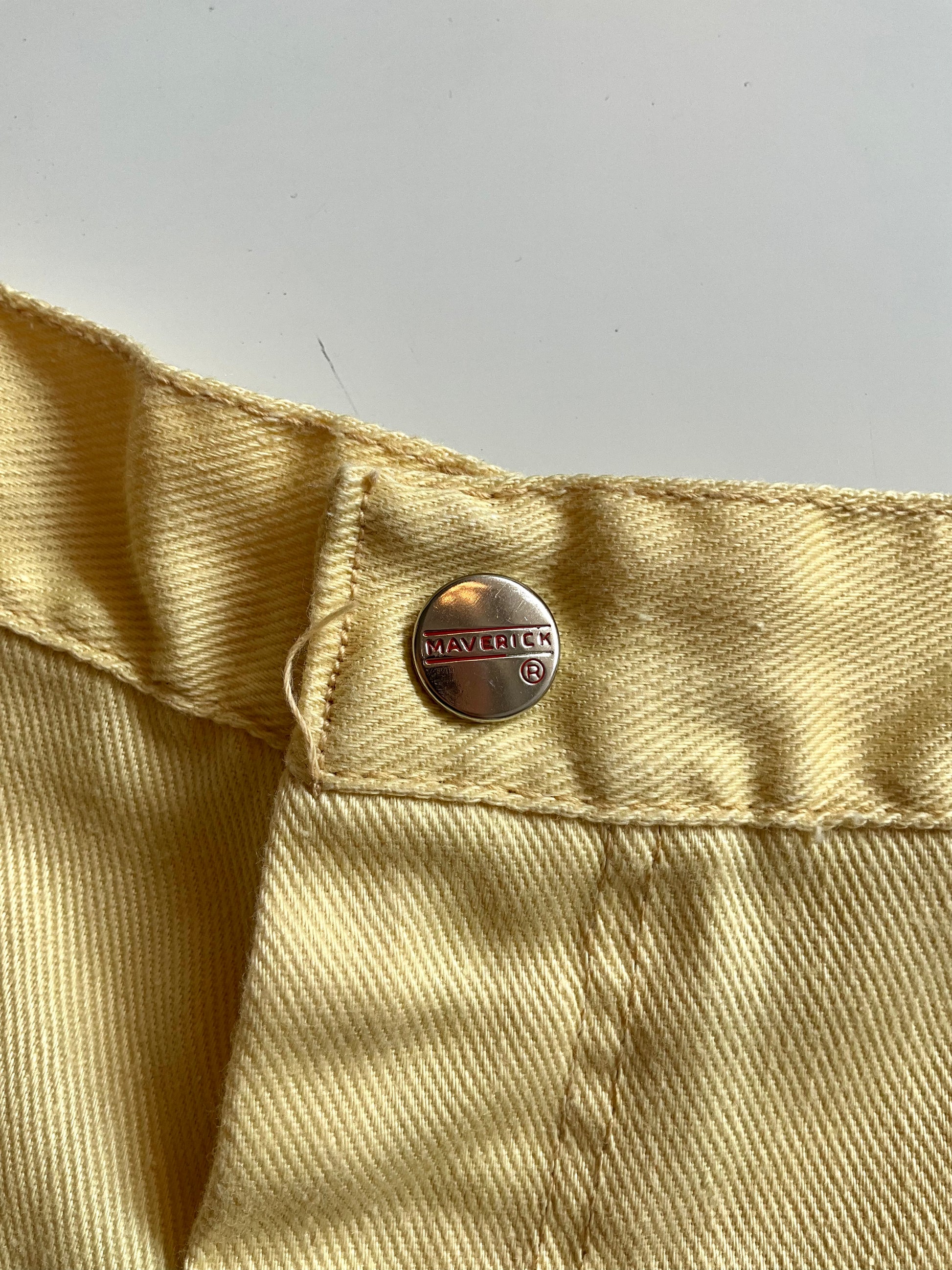 Close-up of yellow fabric with a metal button featuring a Maverick brand logo.