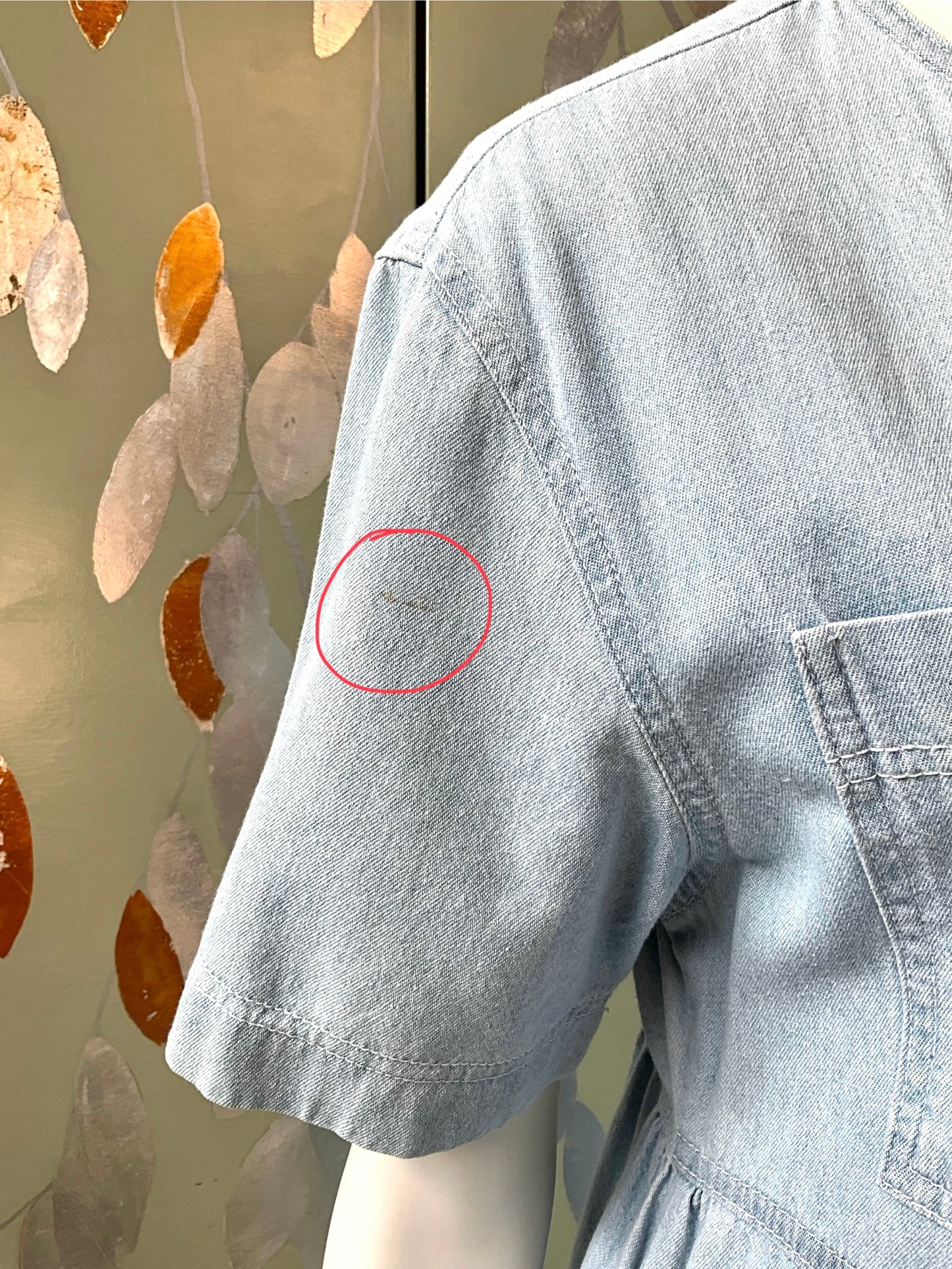 Blue dress with a red circle highlighting a stain on the sleeve against a decorative background.