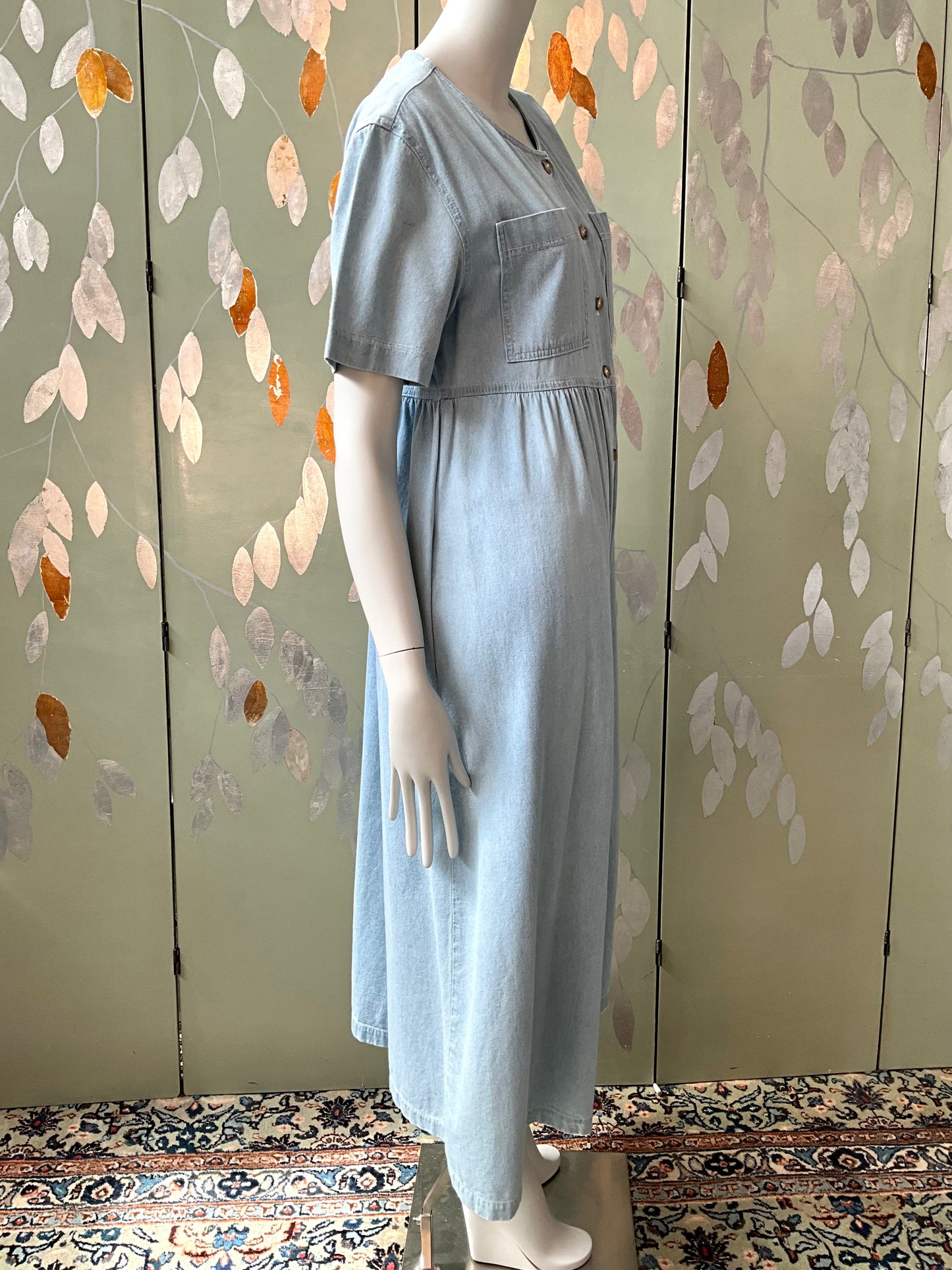Mannequin wearing a light blue dress against a floral-patterned wall.