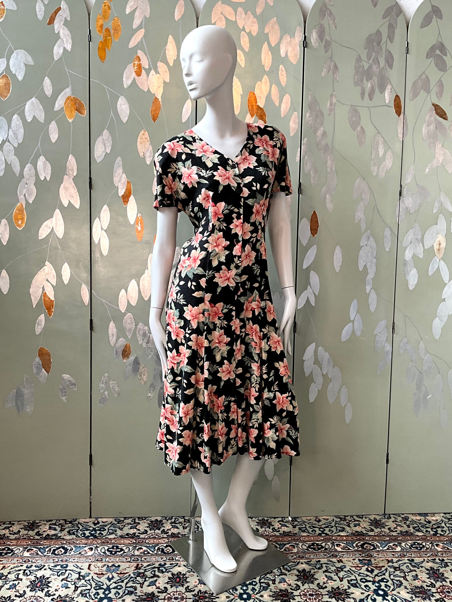 Mannequin wearing a floral dress against a decorative wall with leaf patterns.