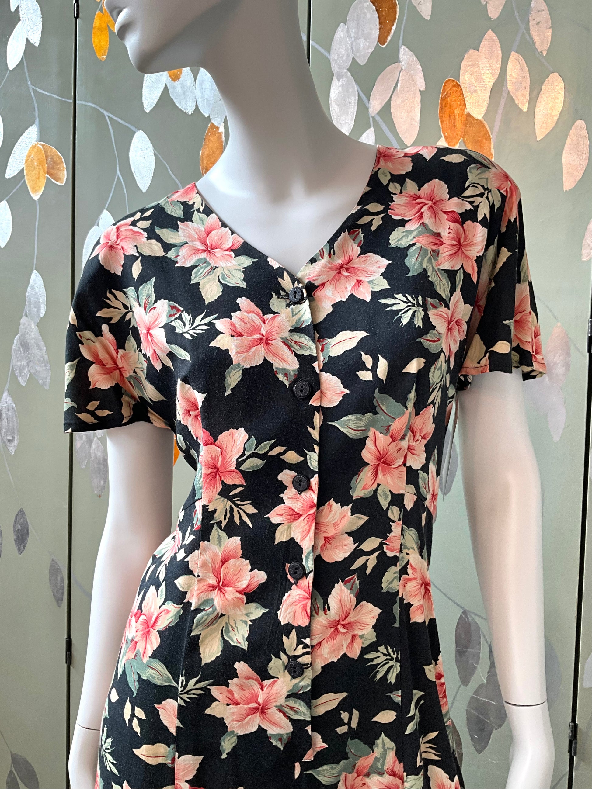 Mannequin wearing a black floral dress with pink and green flowers against a decorative wall.