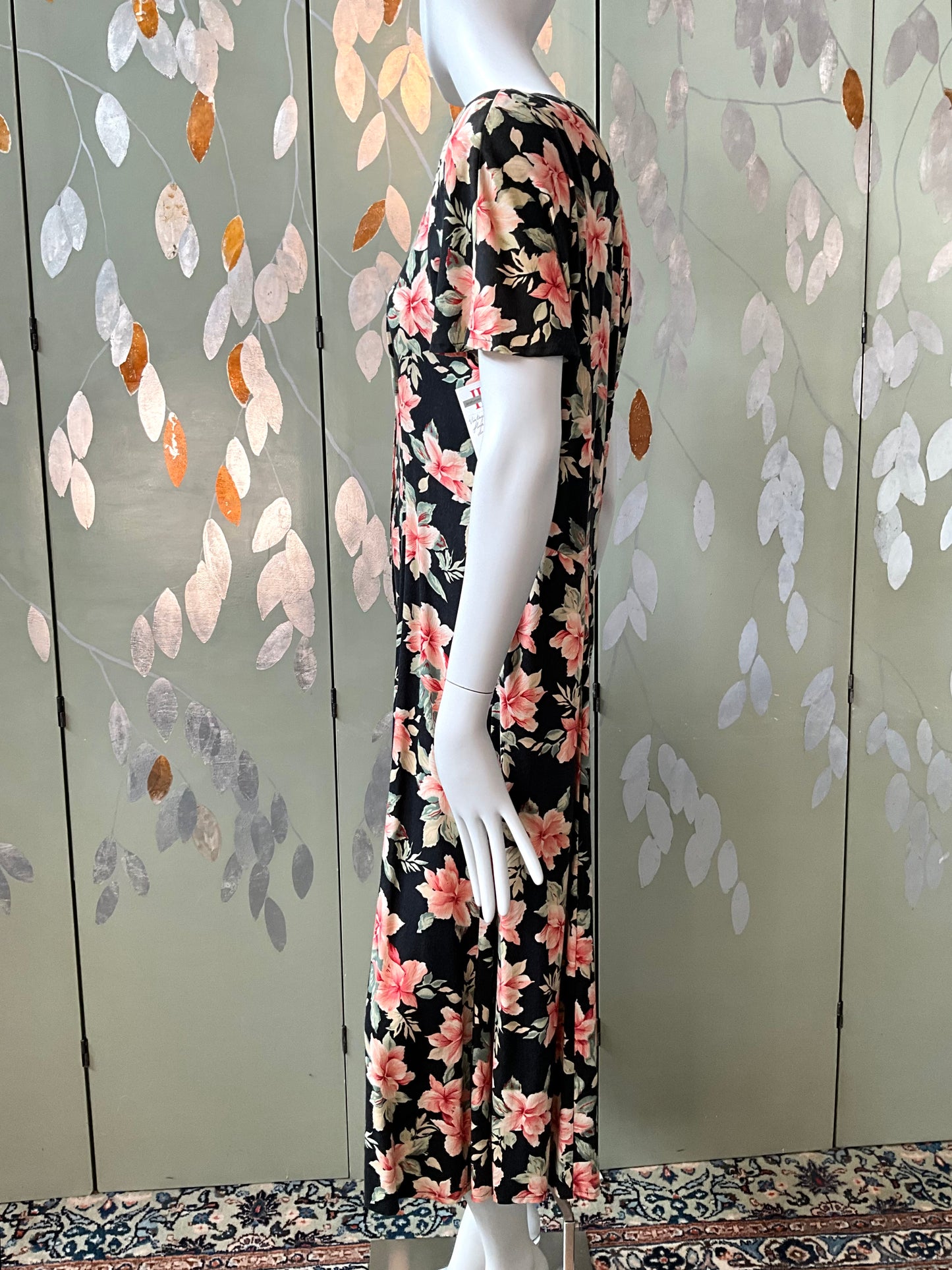 Mannequin wearing a floral dress against a decorative wall with leaf patterns.