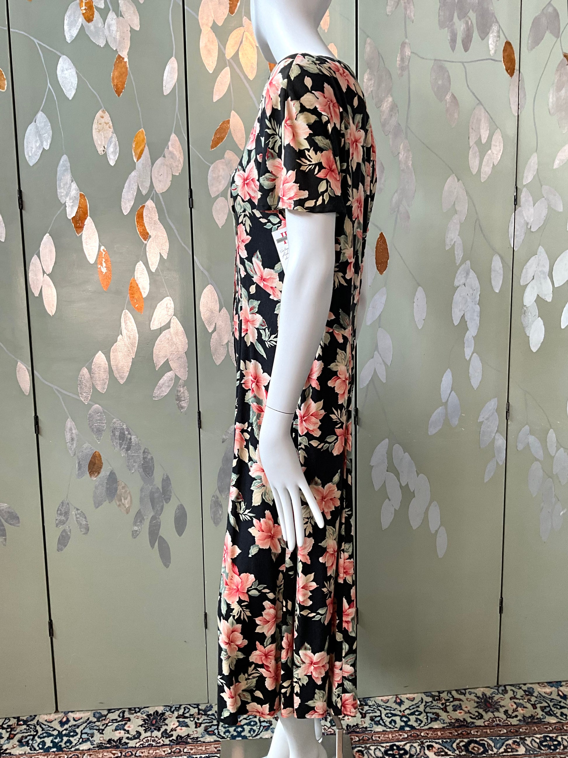 Mannequin wearing a floral dress against a decorative wall with leaf patterns.