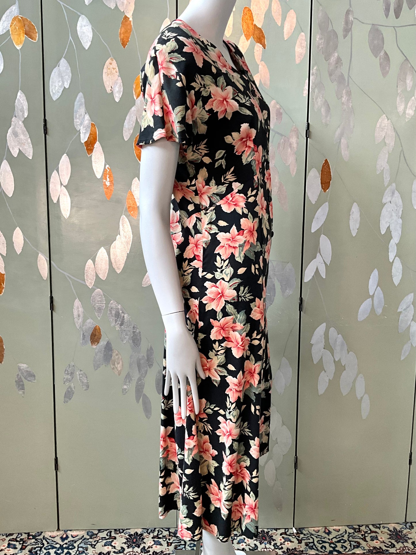 Mannequin wearing a floral dress against a decorative wall with leaf patterns.