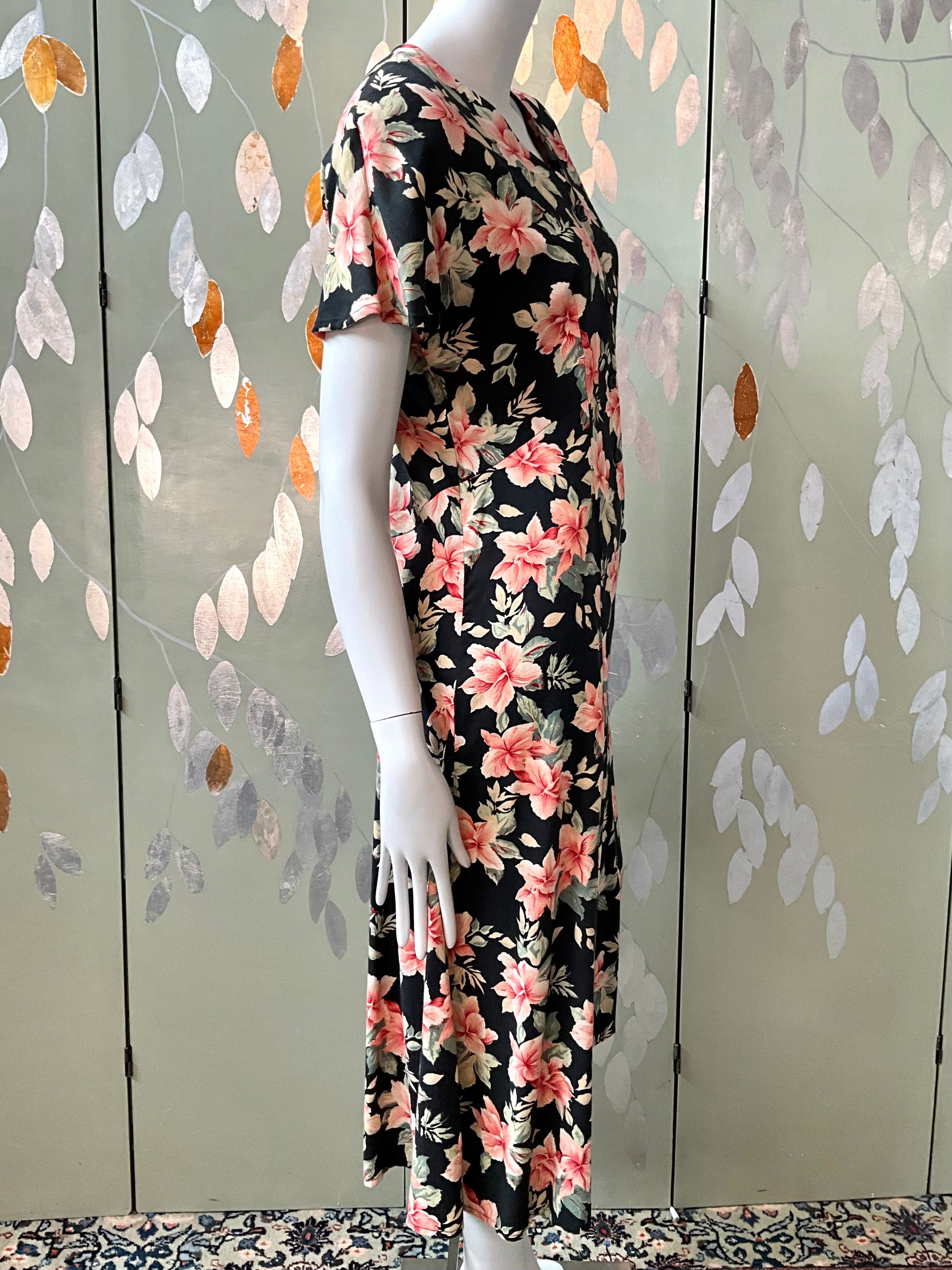 Mannequin wearing a floral dress against a decorative wall with leaf patterns.