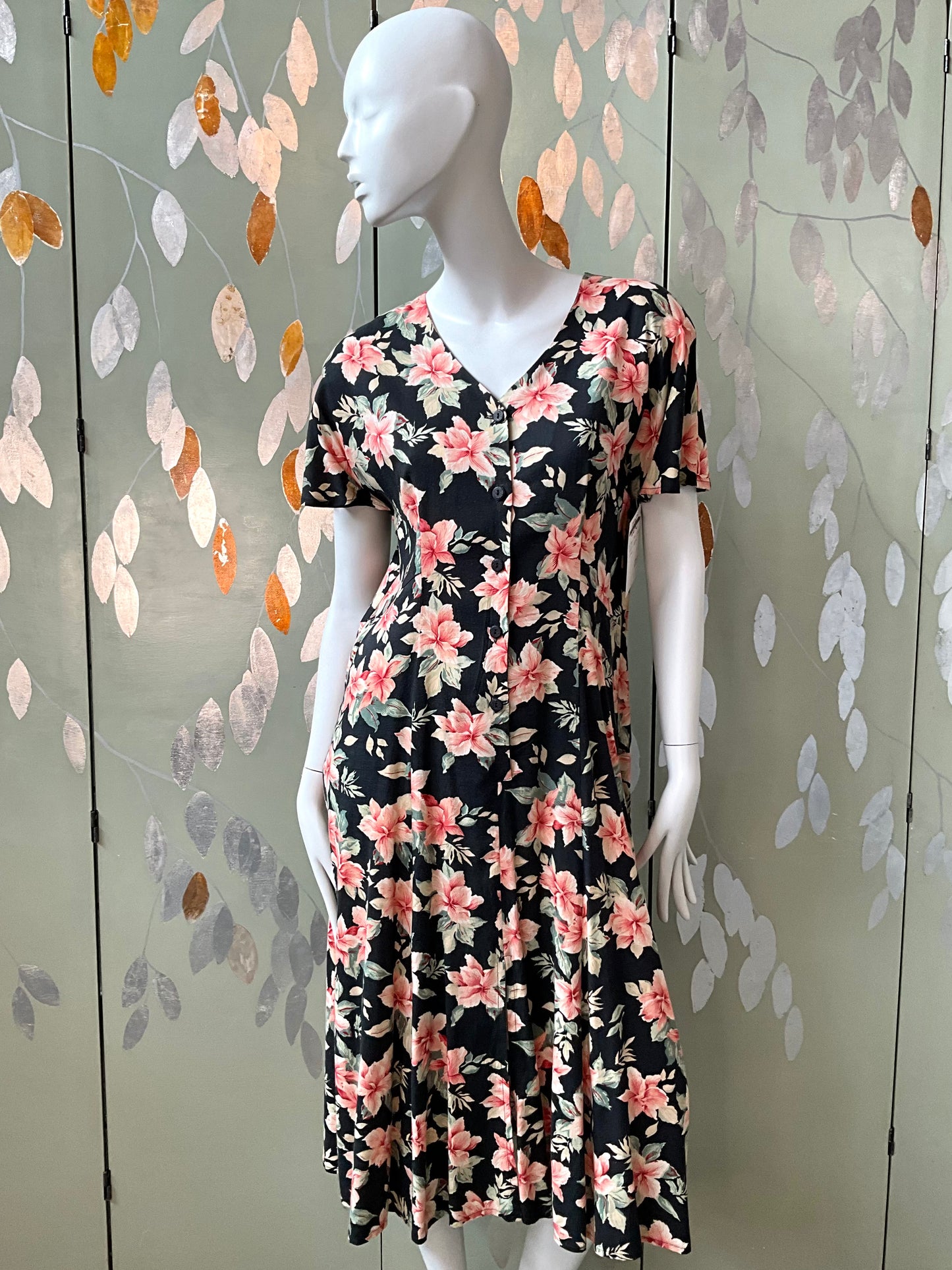 Mannequin wearing a floral dress against a decorative leaf-patterned wall.