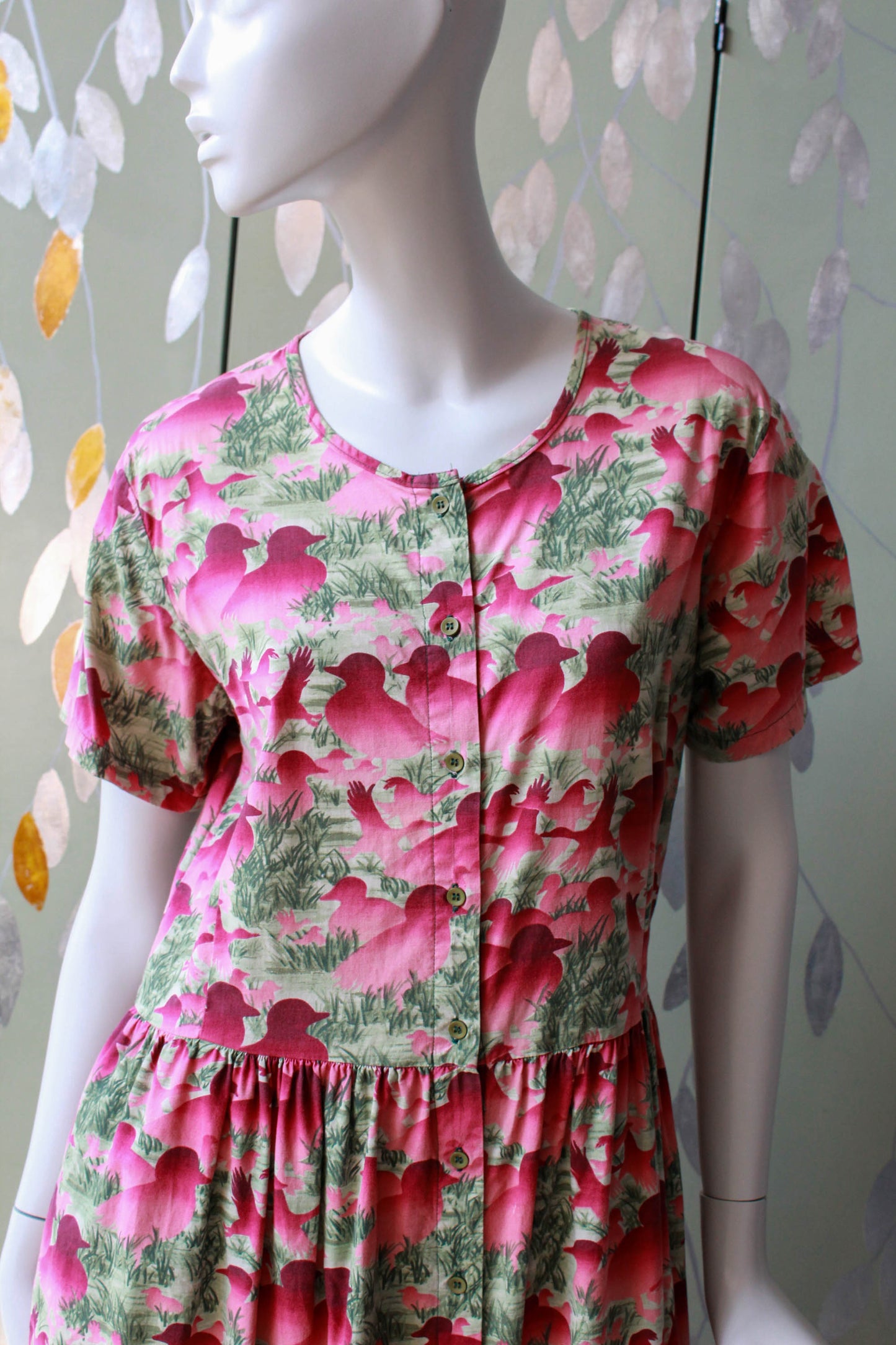 1980s pink duck and bird print against green grass background, short sleeves, button up front, gathered waist midi length skirt with pockets 