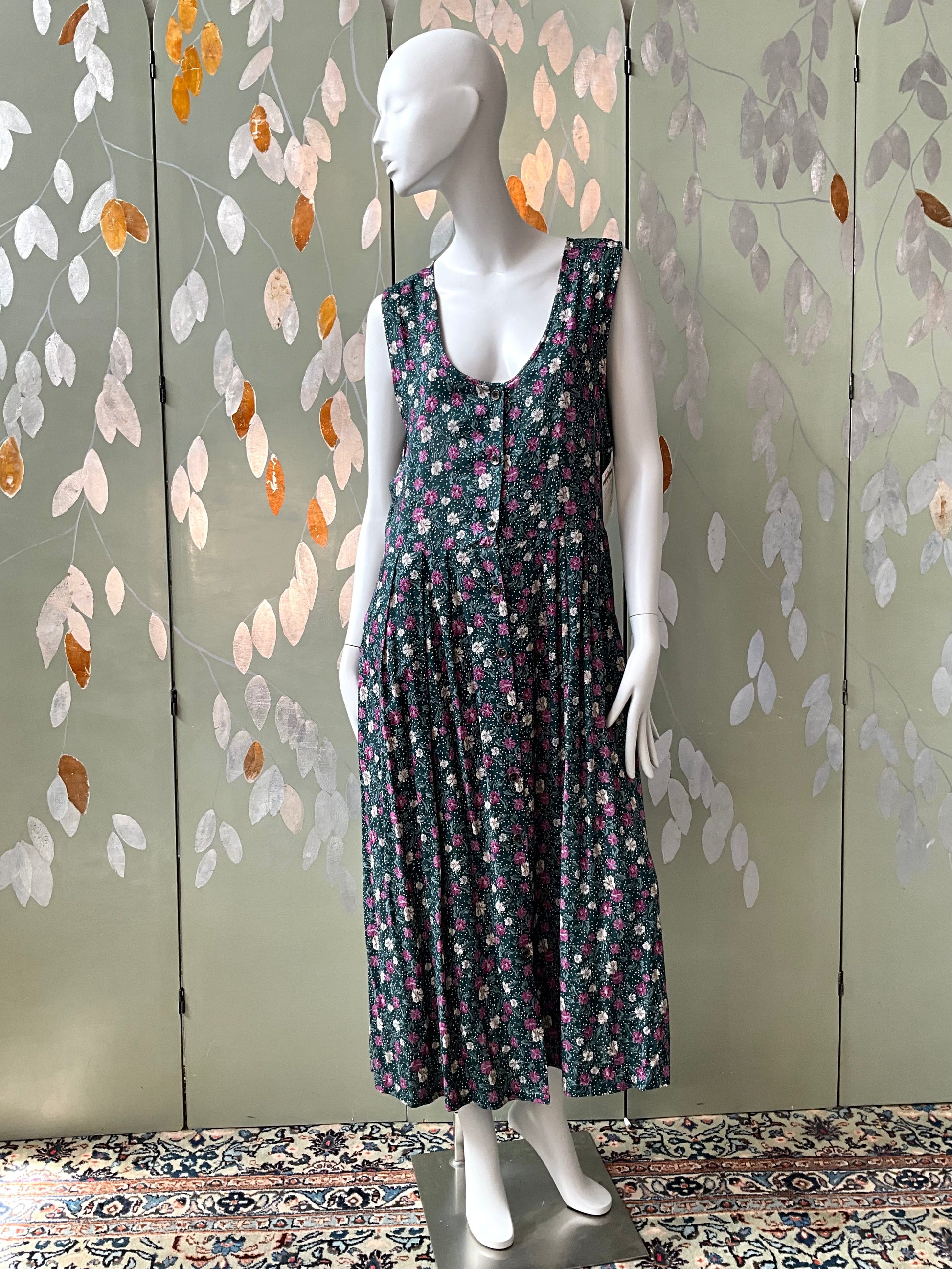 Mannequin wearing a floral dress against a decorative wall with leaf patterns.