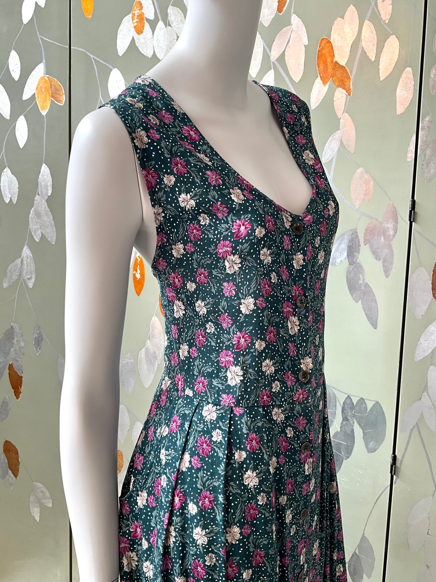 Mannequin wearing a floral dress against a decorative wall with leaf patterns.