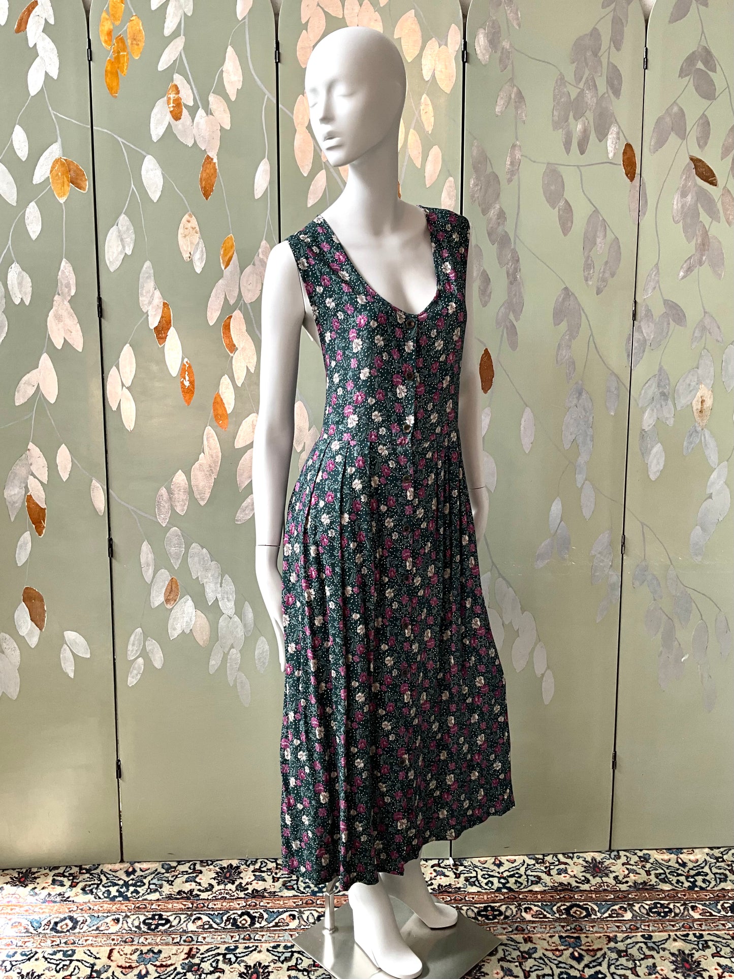 Mannequin wearing a floral dress against a decorative wall with leaf patterns.