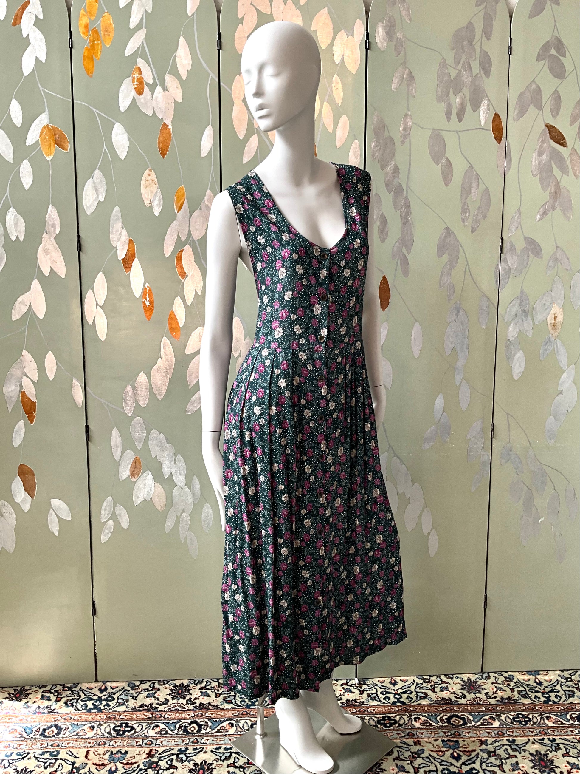 Mannequin wearing a floral dress against a decorative wall with leaf patterns.