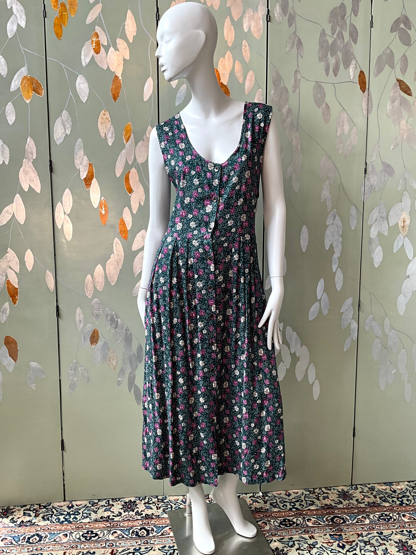 Mannequin wearing a floral dress against a decorative wall with leaf patterns.