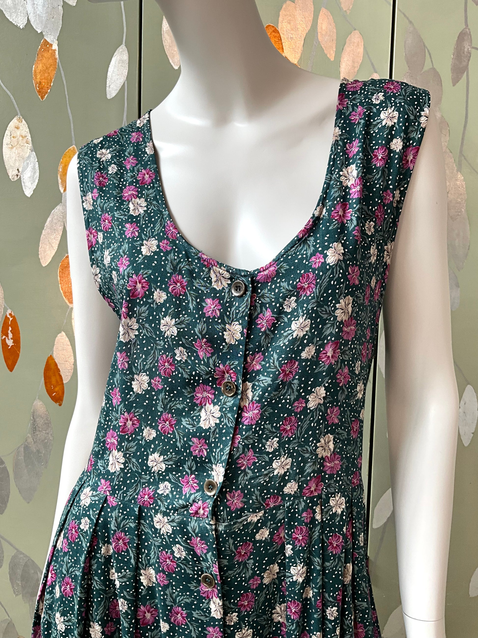 Floral dress on a mannequin against a decorative wall.