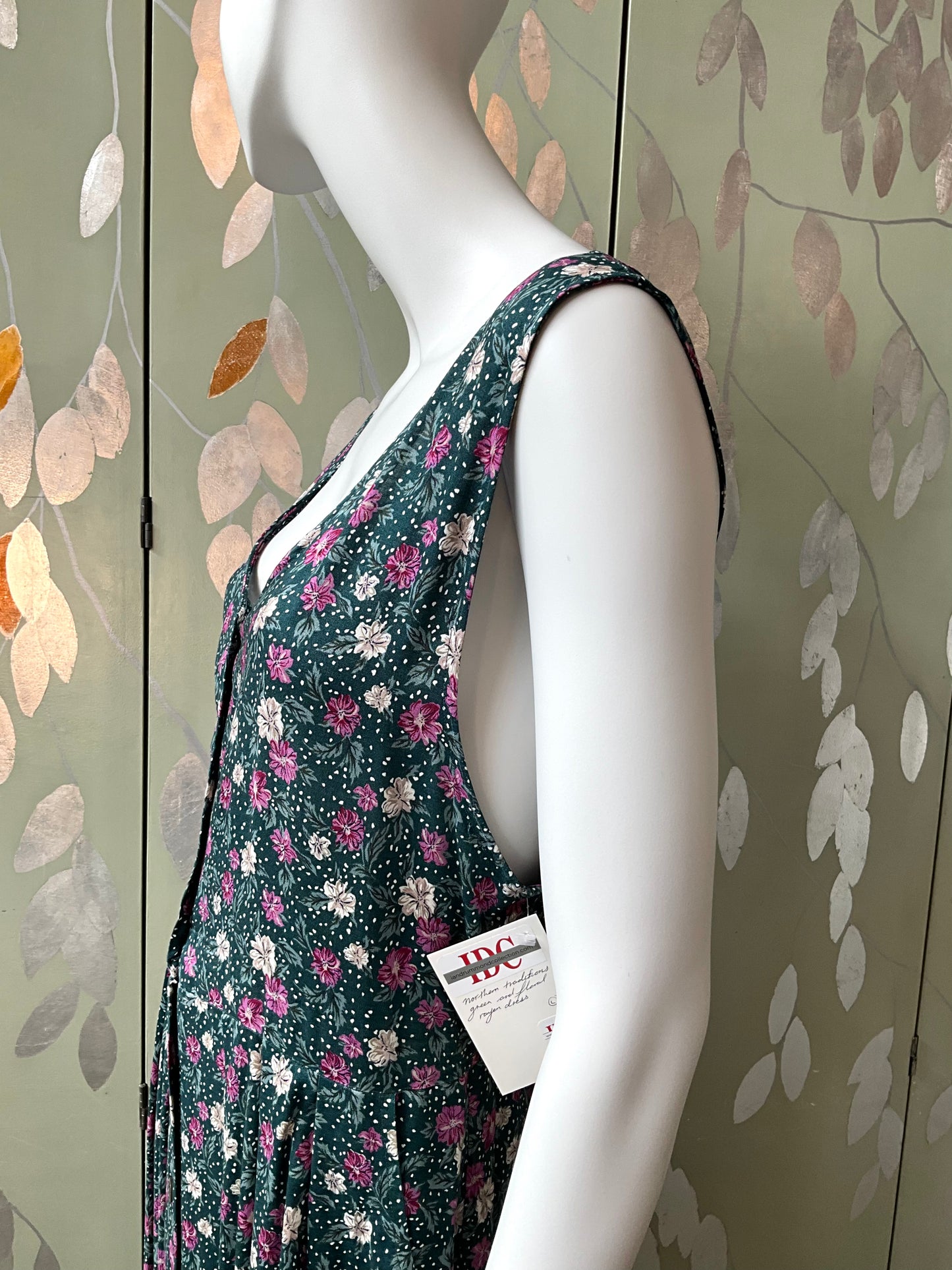 Mannequin wearing a floral dress with a visible brand tag against a decorative wall.