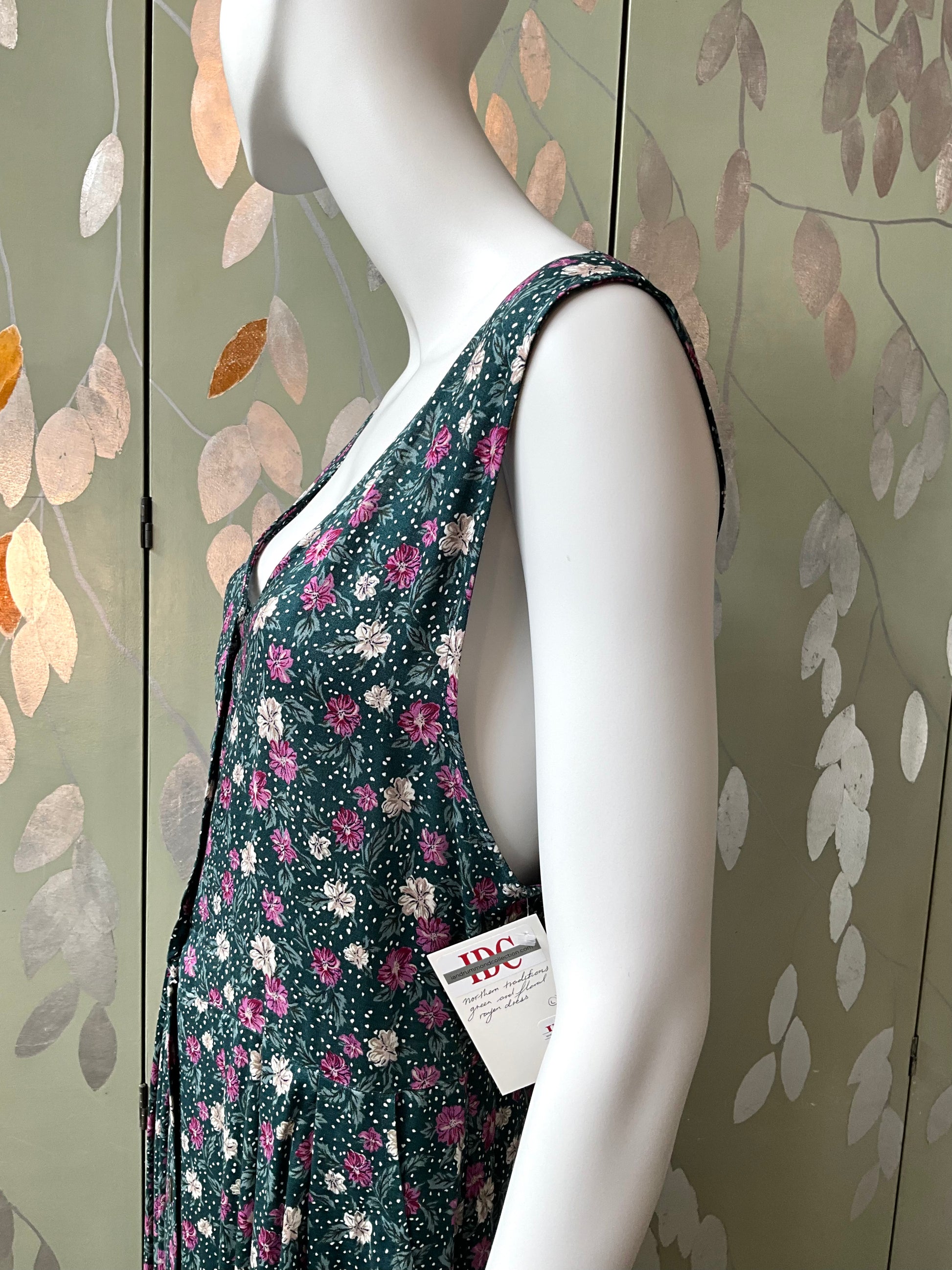 Mannequin wearing a floral dress with a visible brand tag against a decorative wall.